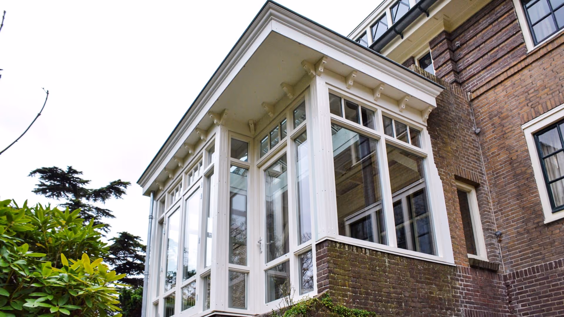 Klassieke witte serre aanbouw met grote raampartijen aan een bakstenen villa in Heemstede
