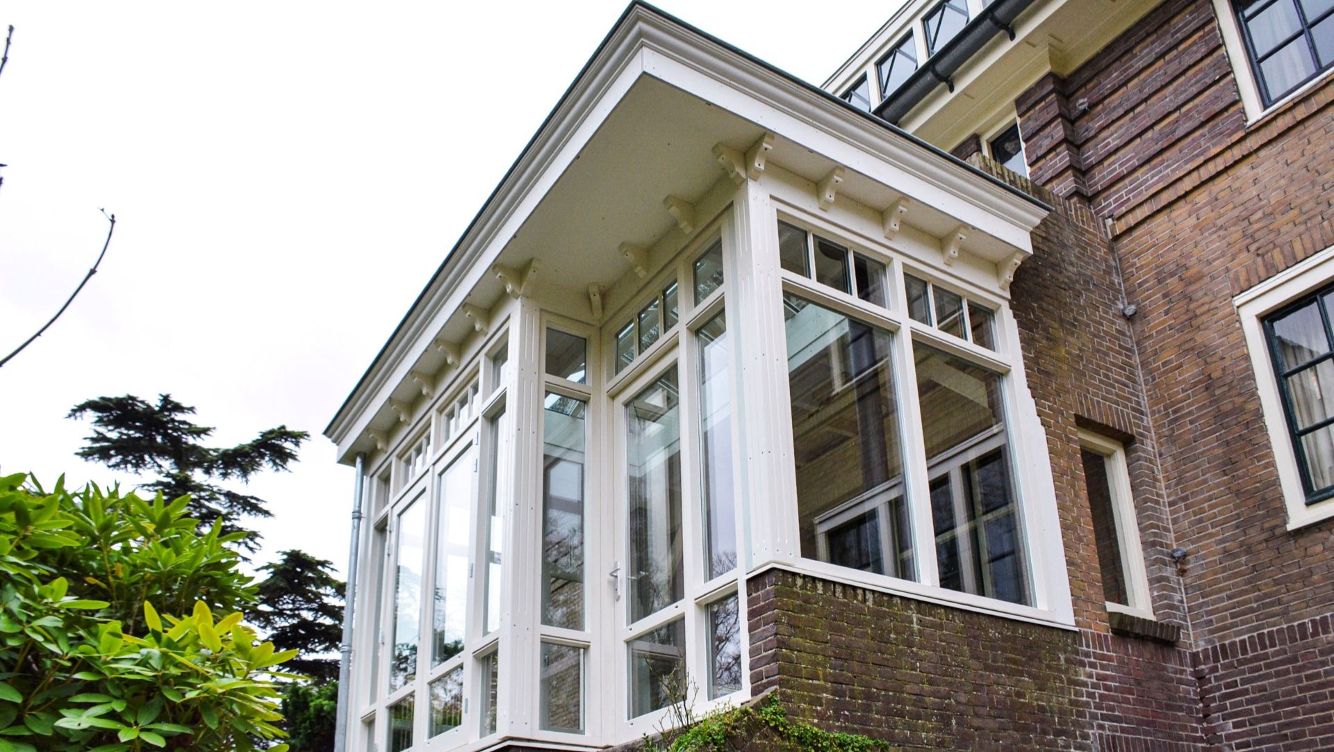 Klassieke witte serre aanbouw met grote raampartijen aan een bakstenen villa in Heemstede