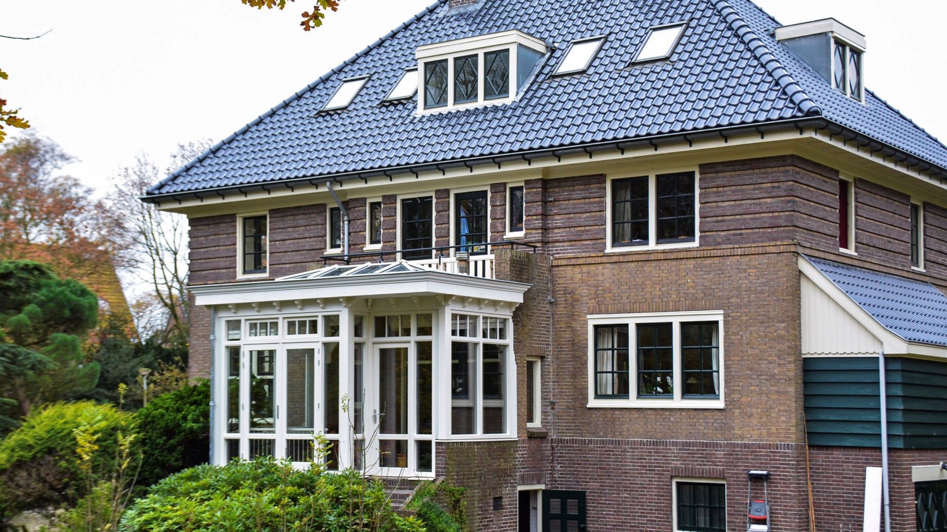 Overzicht van villa met witte serre aanbouw en balkon, gelegen in een groene omgeving in Heemstede