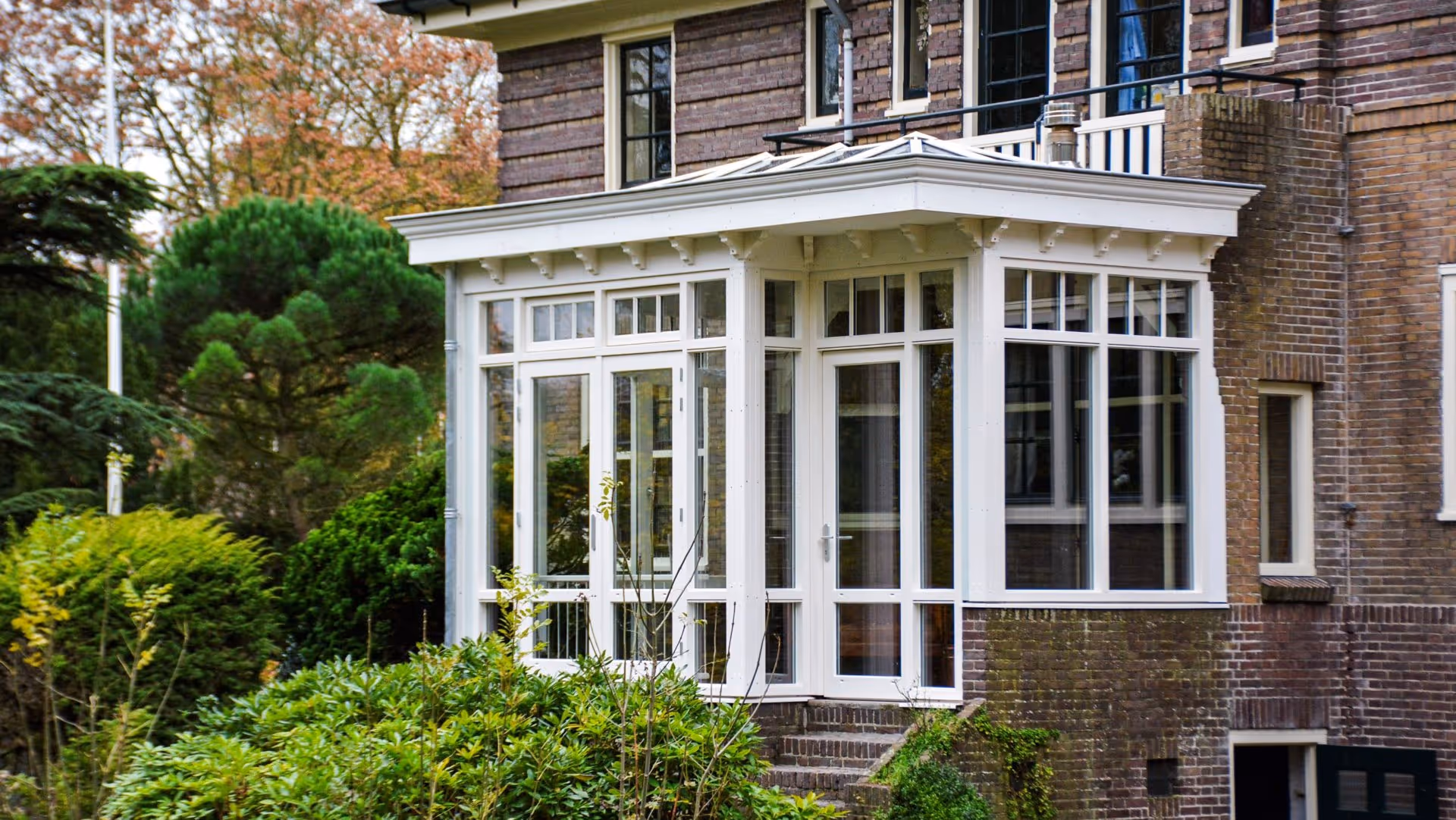 Stijlvolle serre aanbouw met houten kozijnen en grote ramen, omringd door groene tuin in Heemstede