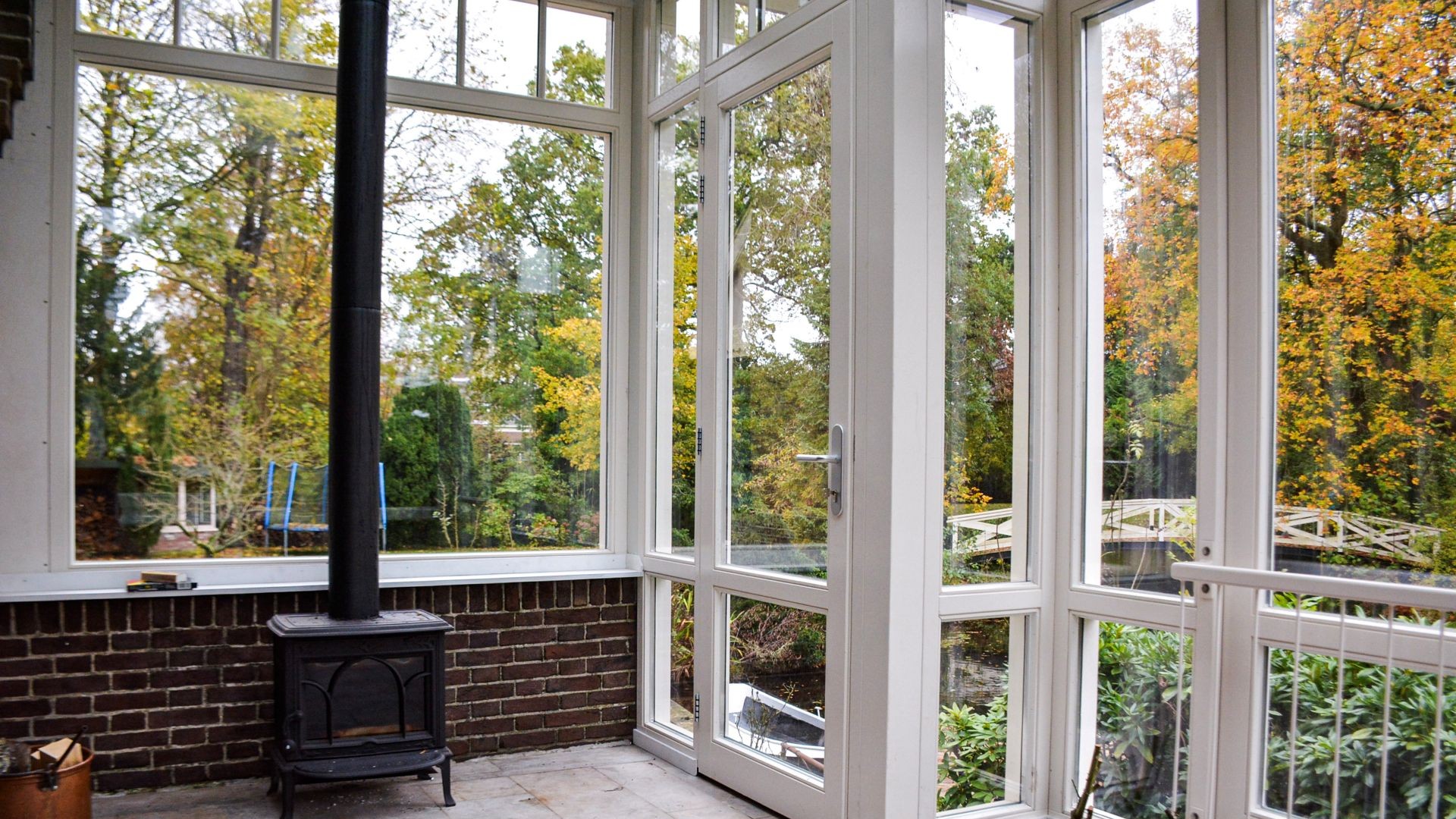 Interieur van serre met houtkachel en uitzicht op groene tuin en waterpartij