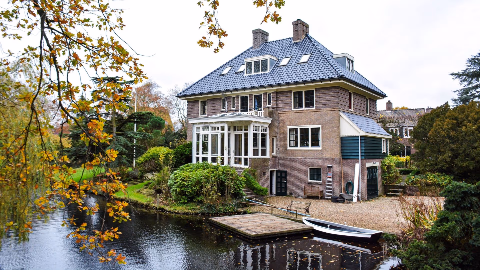 Villa met serre en tuin aan het water, met houten steiger en boot in Heemstede