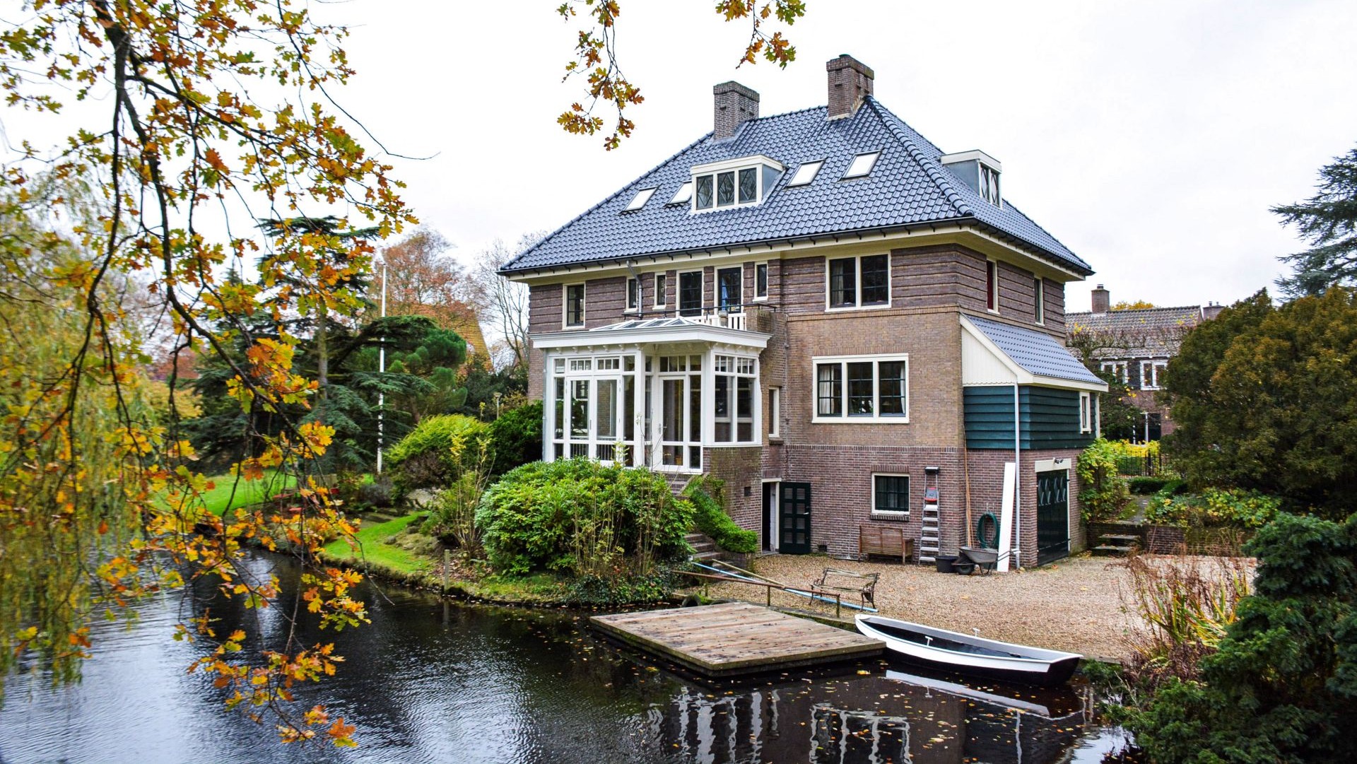 Villa met serre en tuin aan het water, met houten steiger en boot in Heemstede