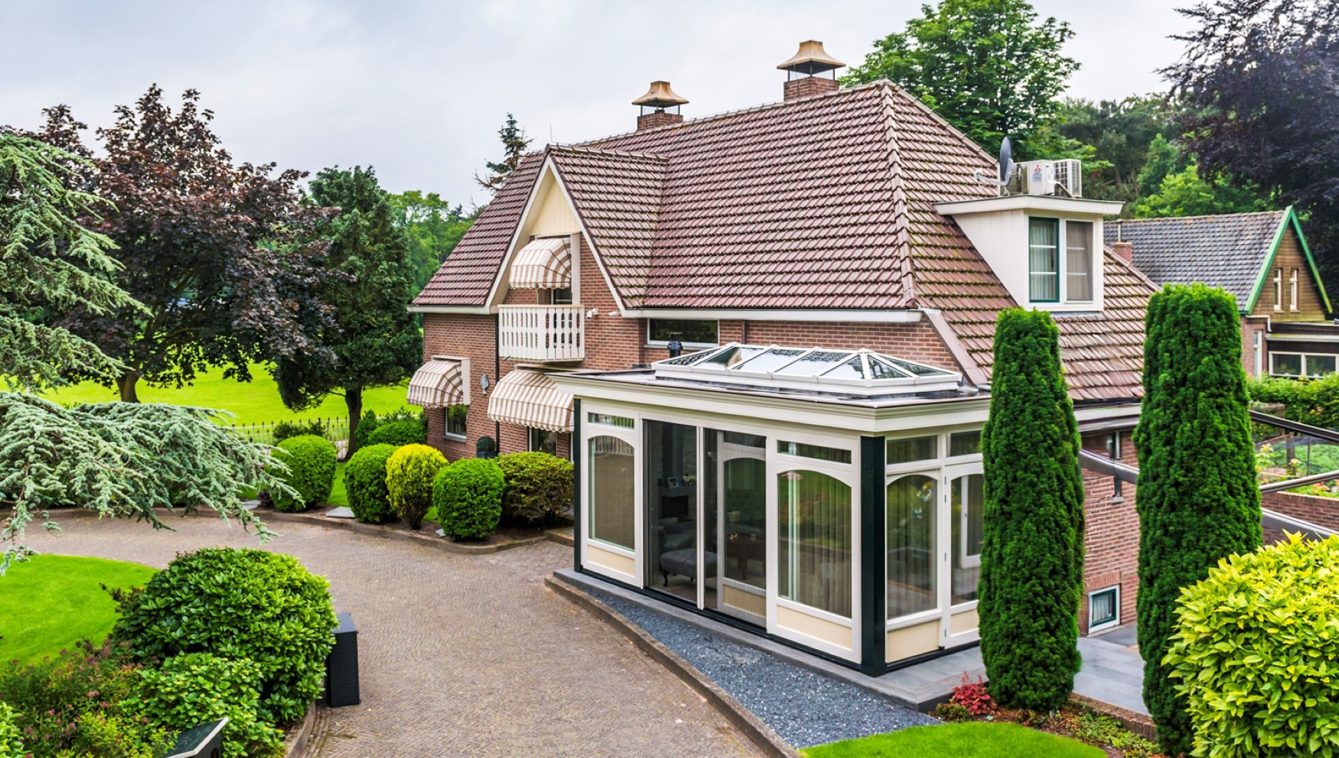 Overzicht van woning met serre aanbouw, glazen dak en groene tuinomgeving