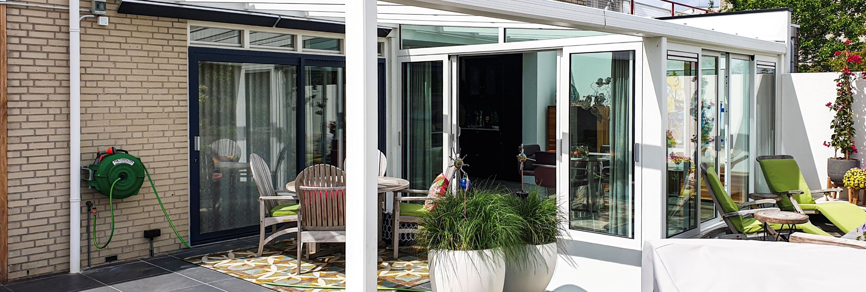 Aluminium tuinkamer met glazen dak en schuifwanden, geplaatst aan moderne woning met ruim terras en groene tuin.