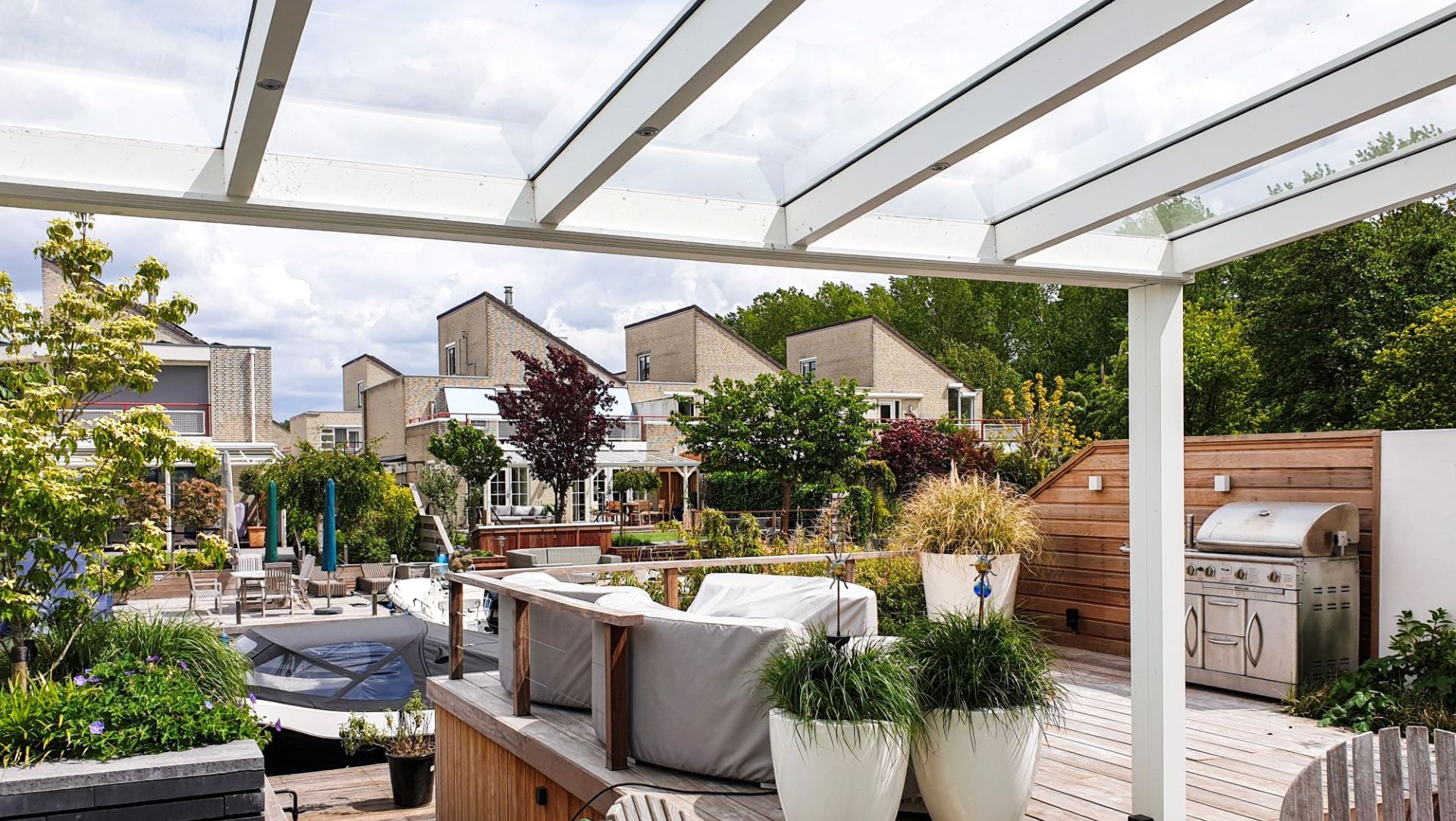 Luxe tuinkamer met glazen dak en open schuifpuien, met zicht op terras met buitenkeuken en groene beplanting.