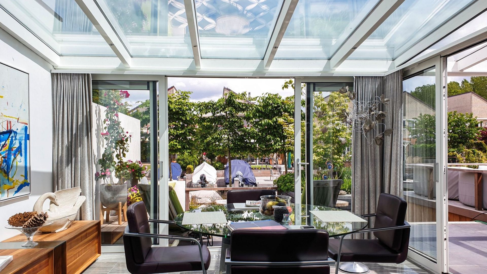 Buitenaanzicht van aluminium tuinkamer met glazen schuifwanden, grenzend aan modern terras met tuinmeubilair en groen.