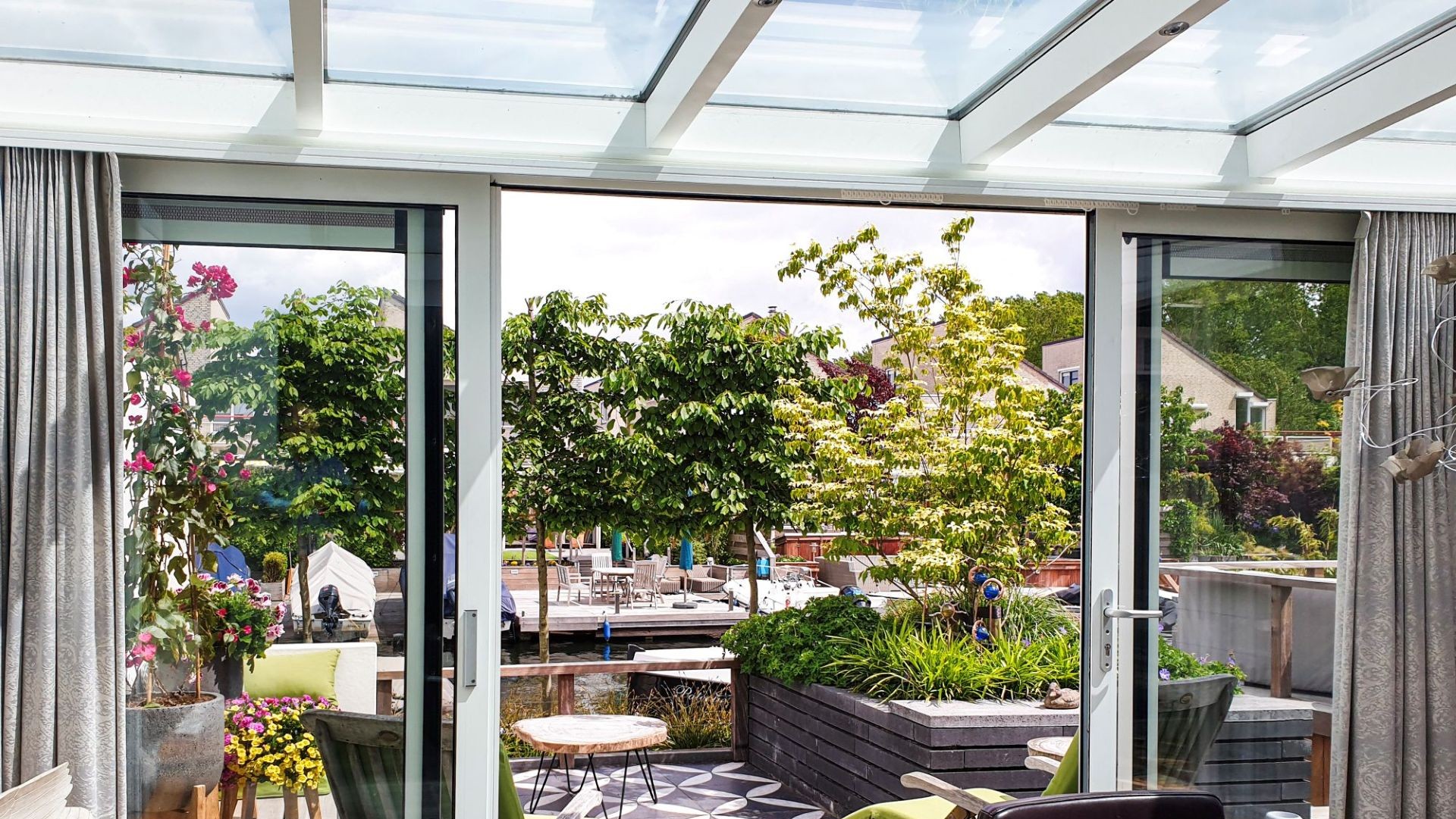 Moderne serre met glazen dak en schuifpuien, ingericht met eettafel en kunst aan de muur, met toegang tot zonnige tuin.