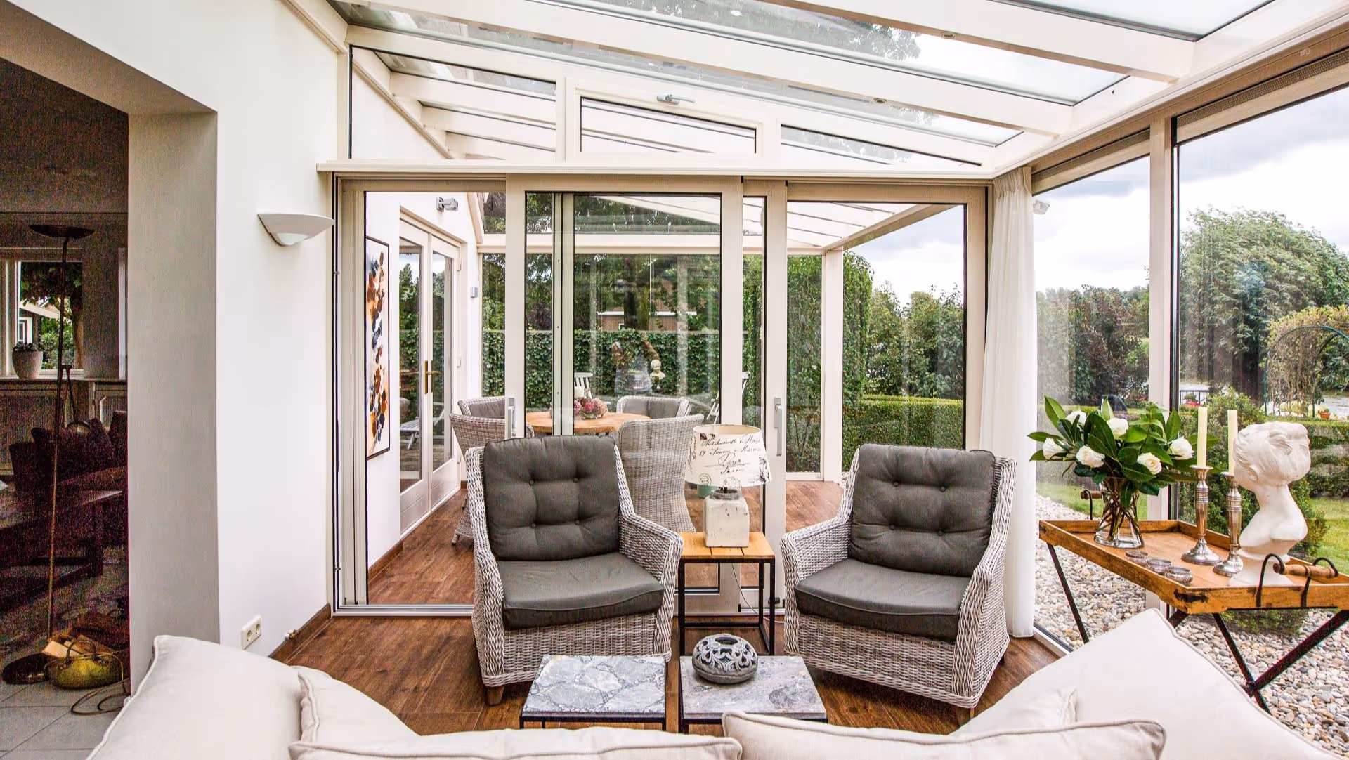 Interieur van de tuinkamer met grote raampartijen en uitzicht op een groene tuin