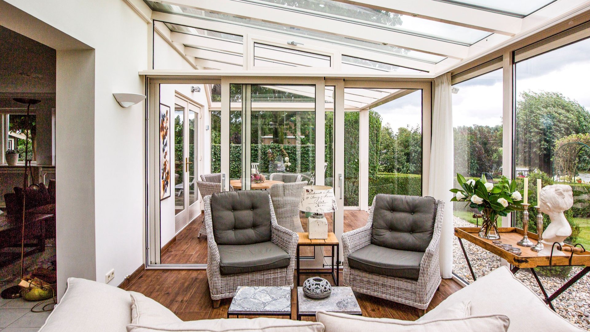 Interieur van de tuinkamer met grote raampartijen en uitzicht op een groene tuin