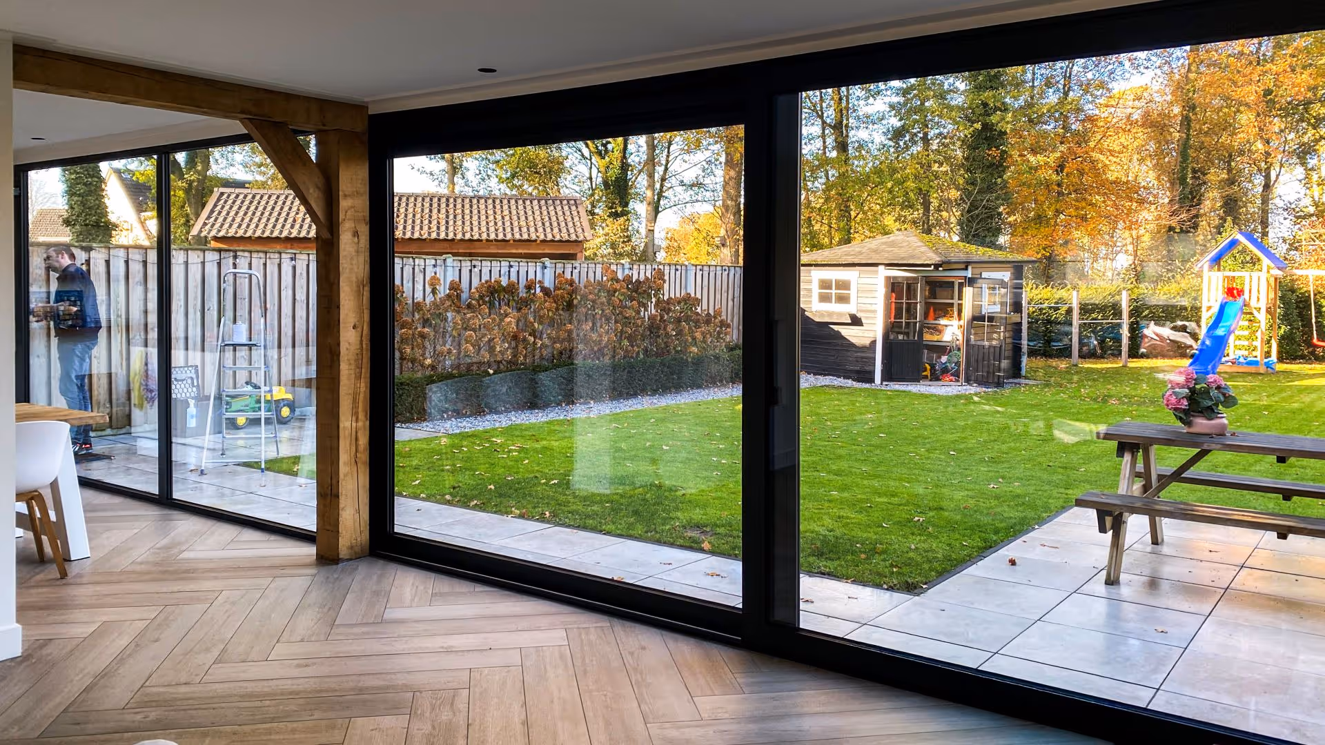 Interieur met grote schuifpuien en zwarte kozijnen die zorgen voor veel lichtinval en zicht op de tuin
