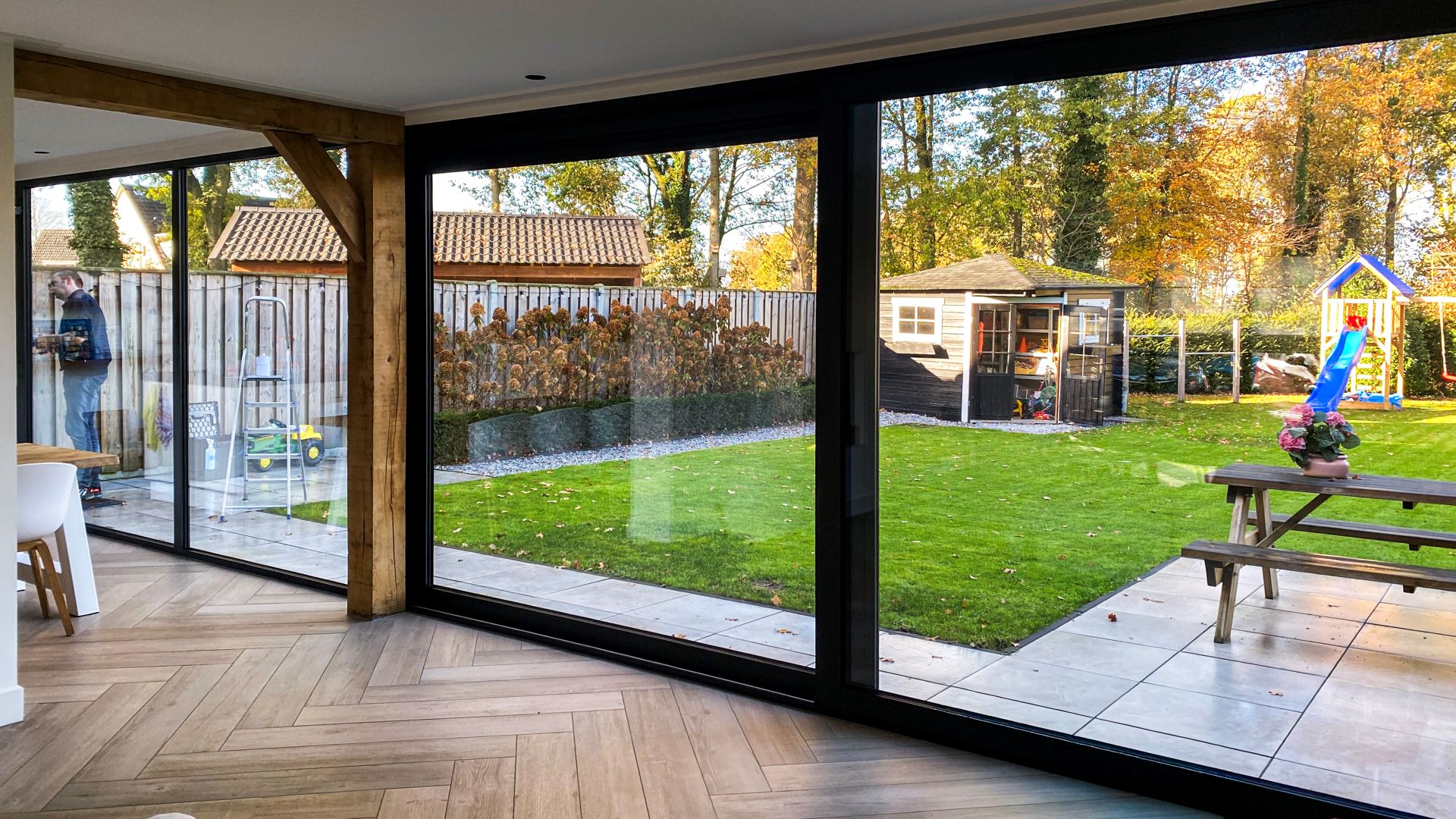 Interieur met grote schuifpuien en zwarte kozijnen die zorgen voor veel lichtinval en zicht op de tuin