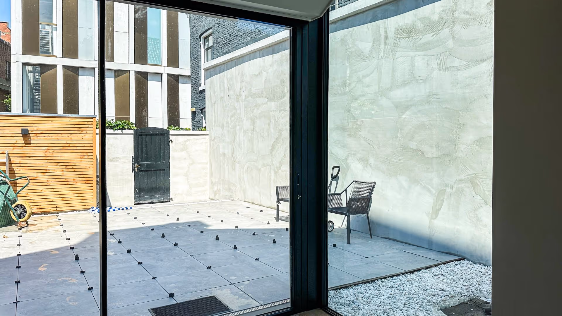 Uitzicht door een minimalistische schuifpui op een betegelde patio met houten schutting