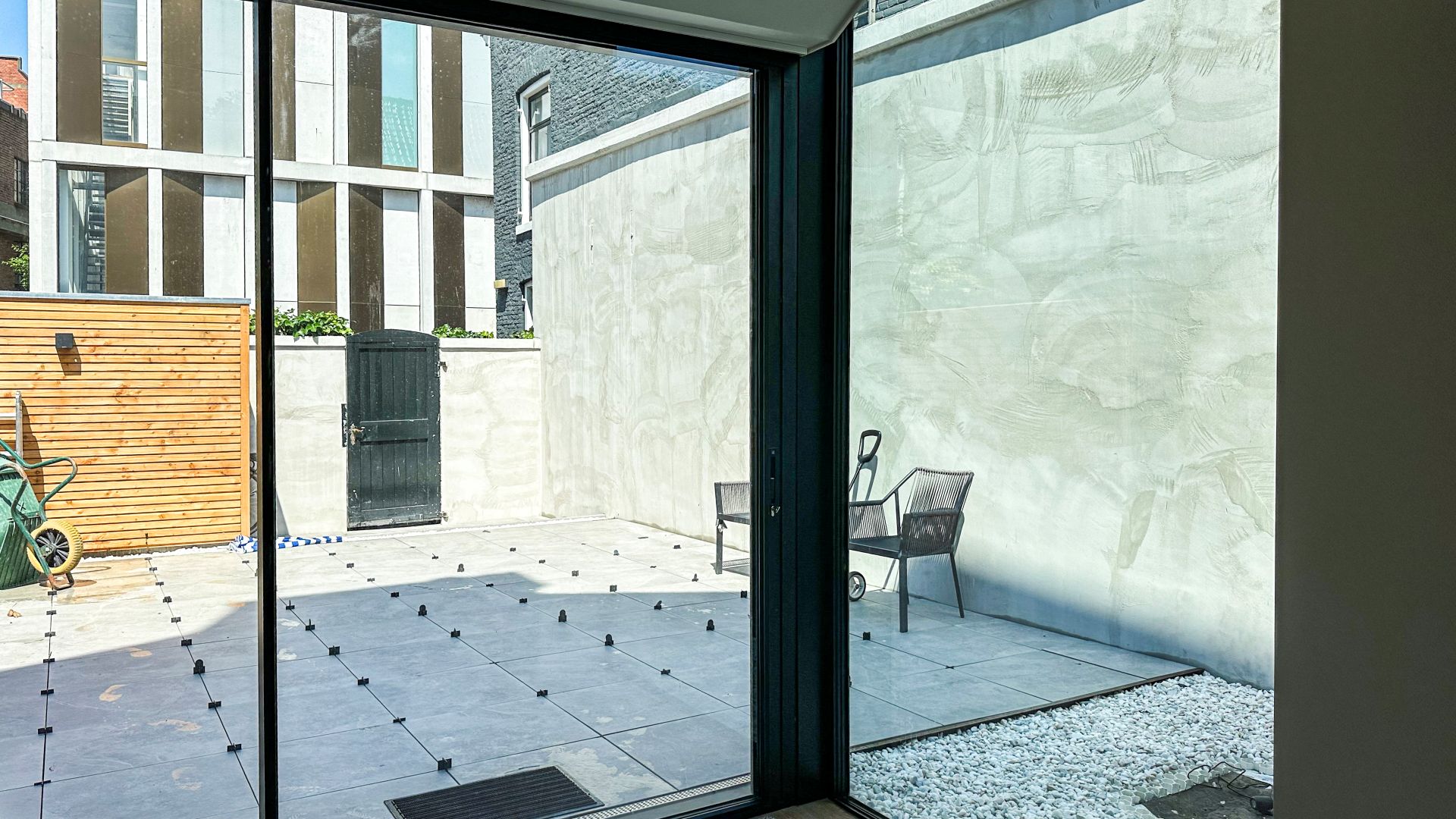 Uitzicht door een minimalistische schuifpui op een betegelde patio met houten schutting