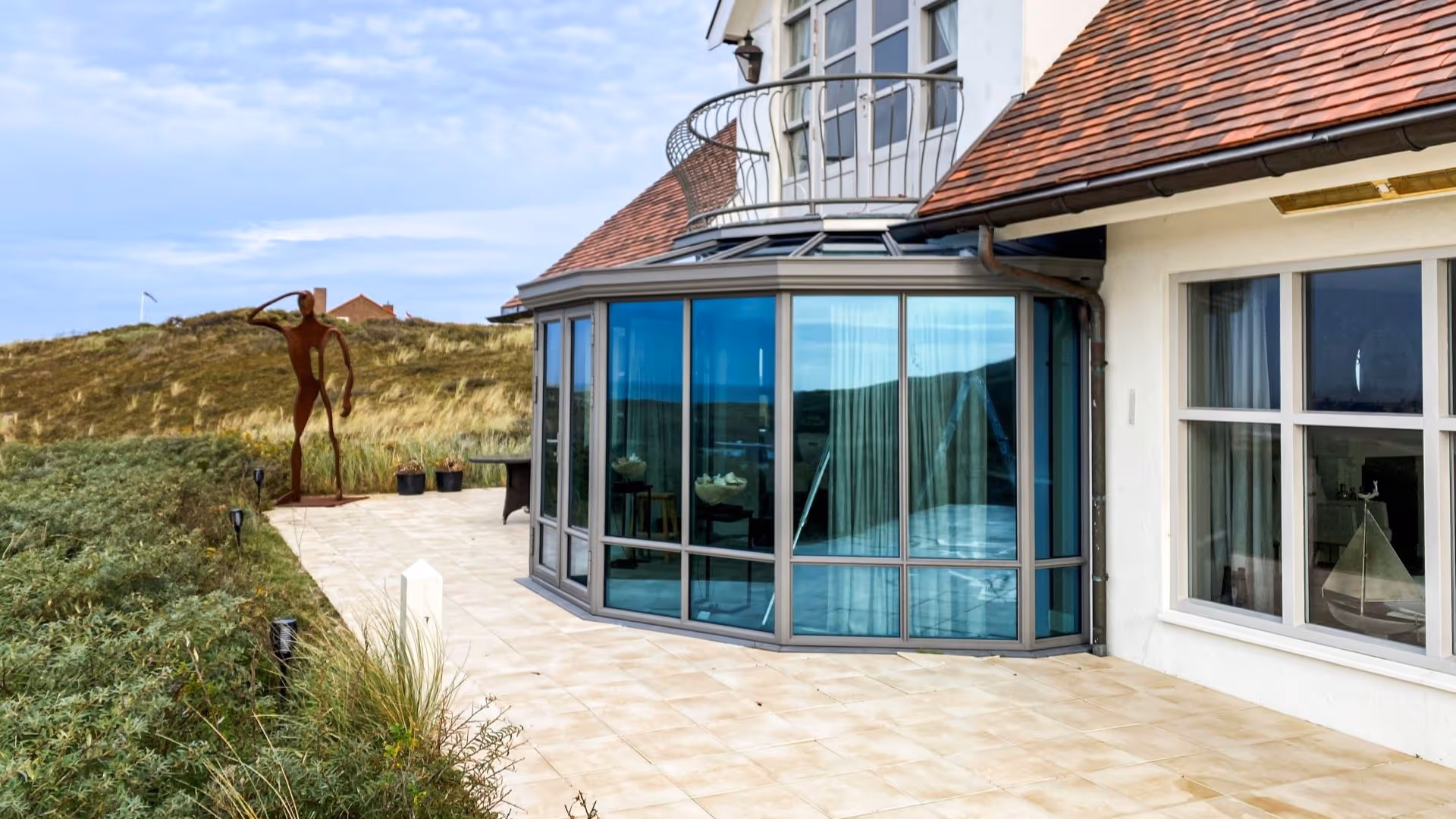 Ronde steellook serre met smalle aluminium profielen en uitzicht op de kust