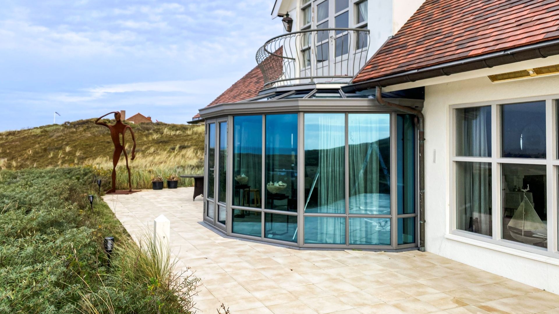 Ronde steellook serre met smalle aluminium profielen en uitzicht op de kust