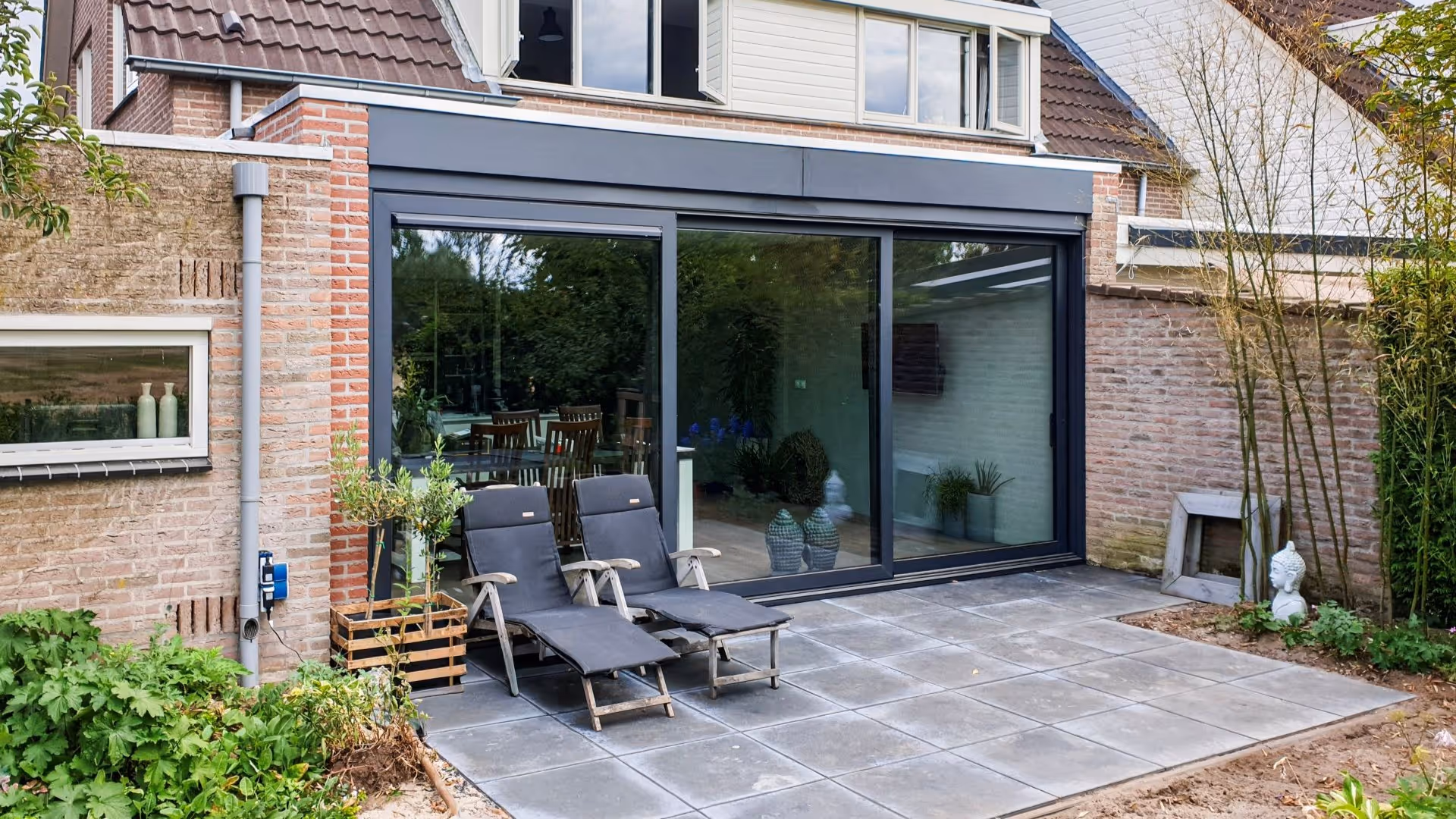 Strakke zwarte serre aanbouw met glazen schuifwand en modern terras in Borculo