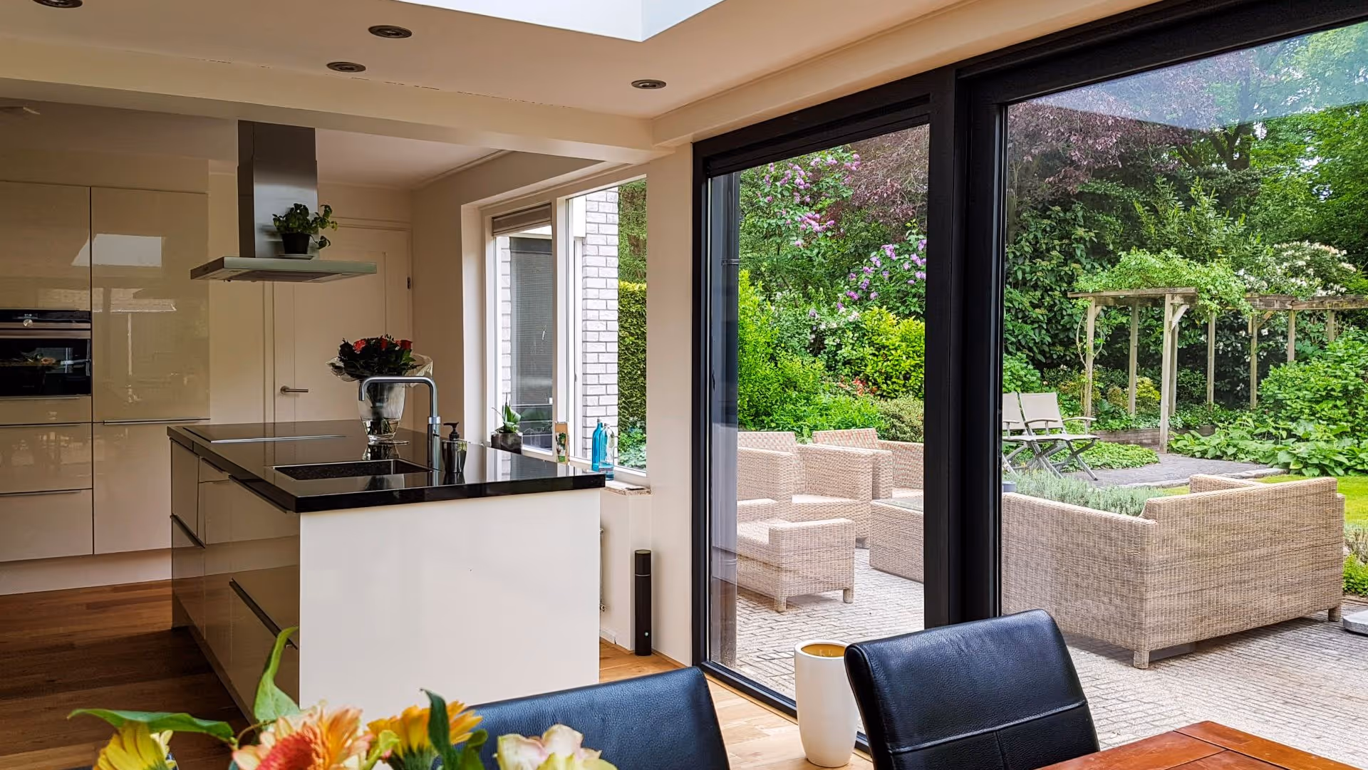 Exclusieve woonkeuken met glazen serre aanbouw en uitzicht op groene tuin