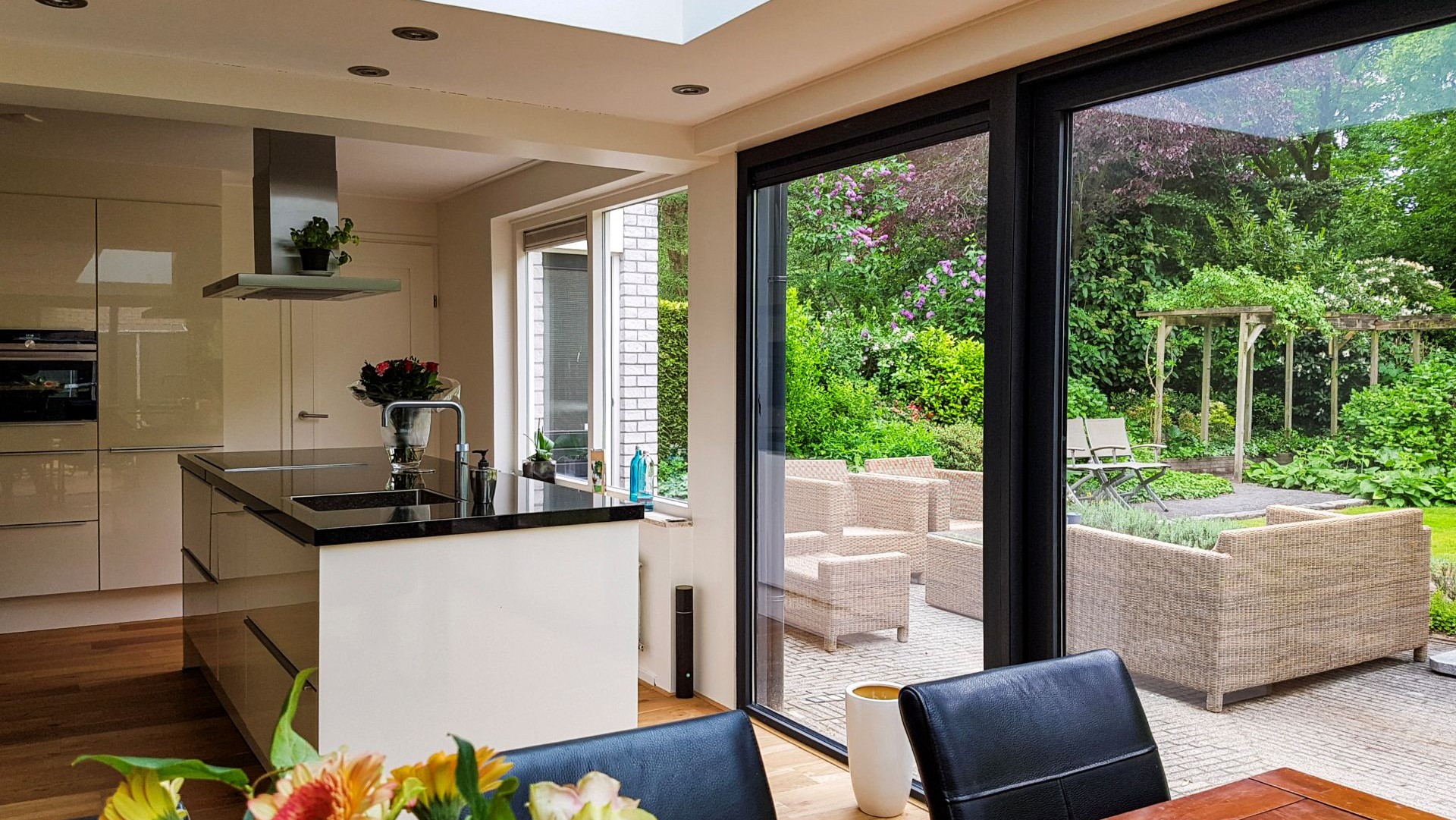 Exclusieve woonkeuken met glazen serre aanbouw en uitzicht op groene tuin