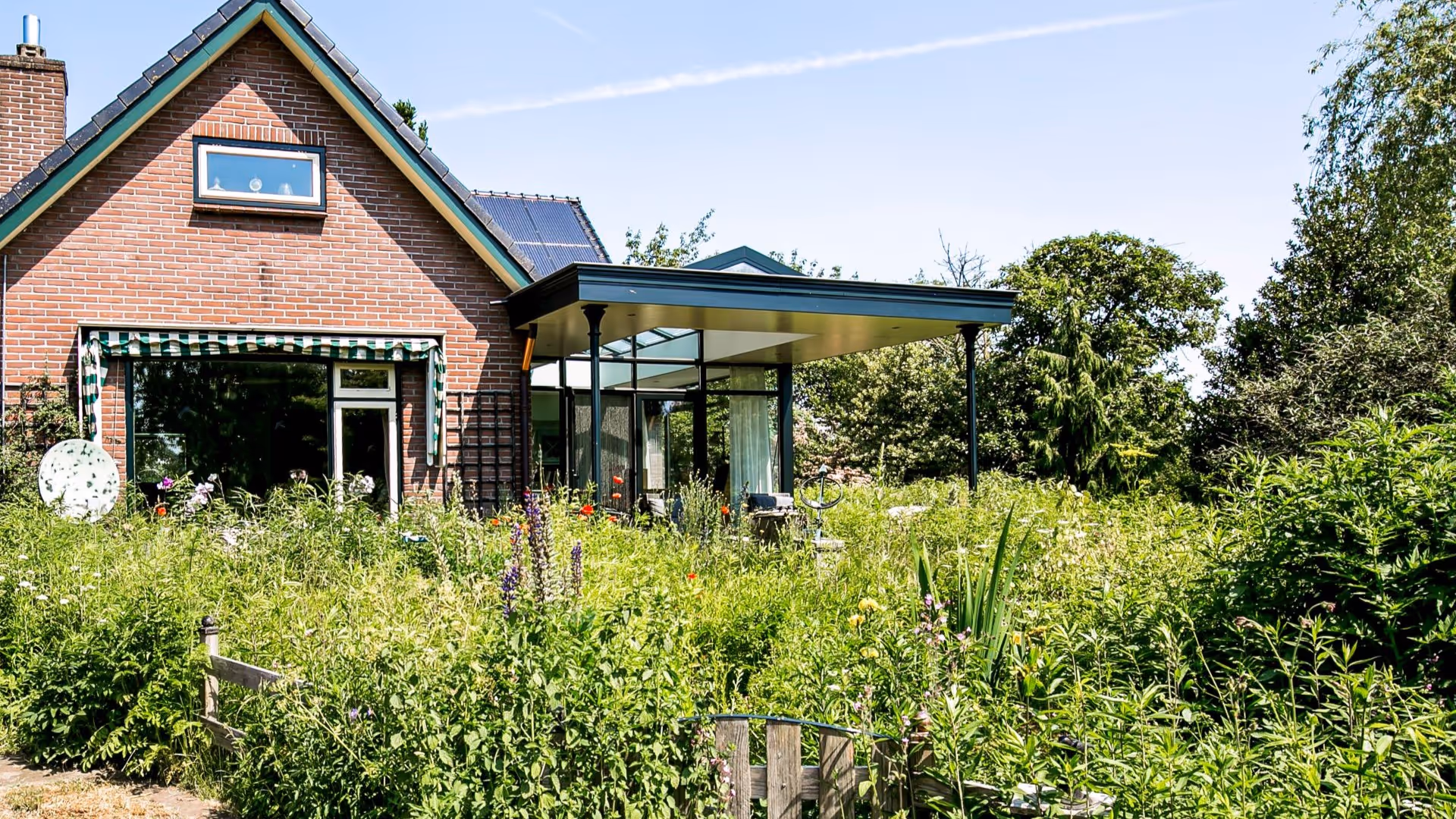 Luxe serre aanbouw met glazen dak en moderne terrasoverkapping in groene tuin