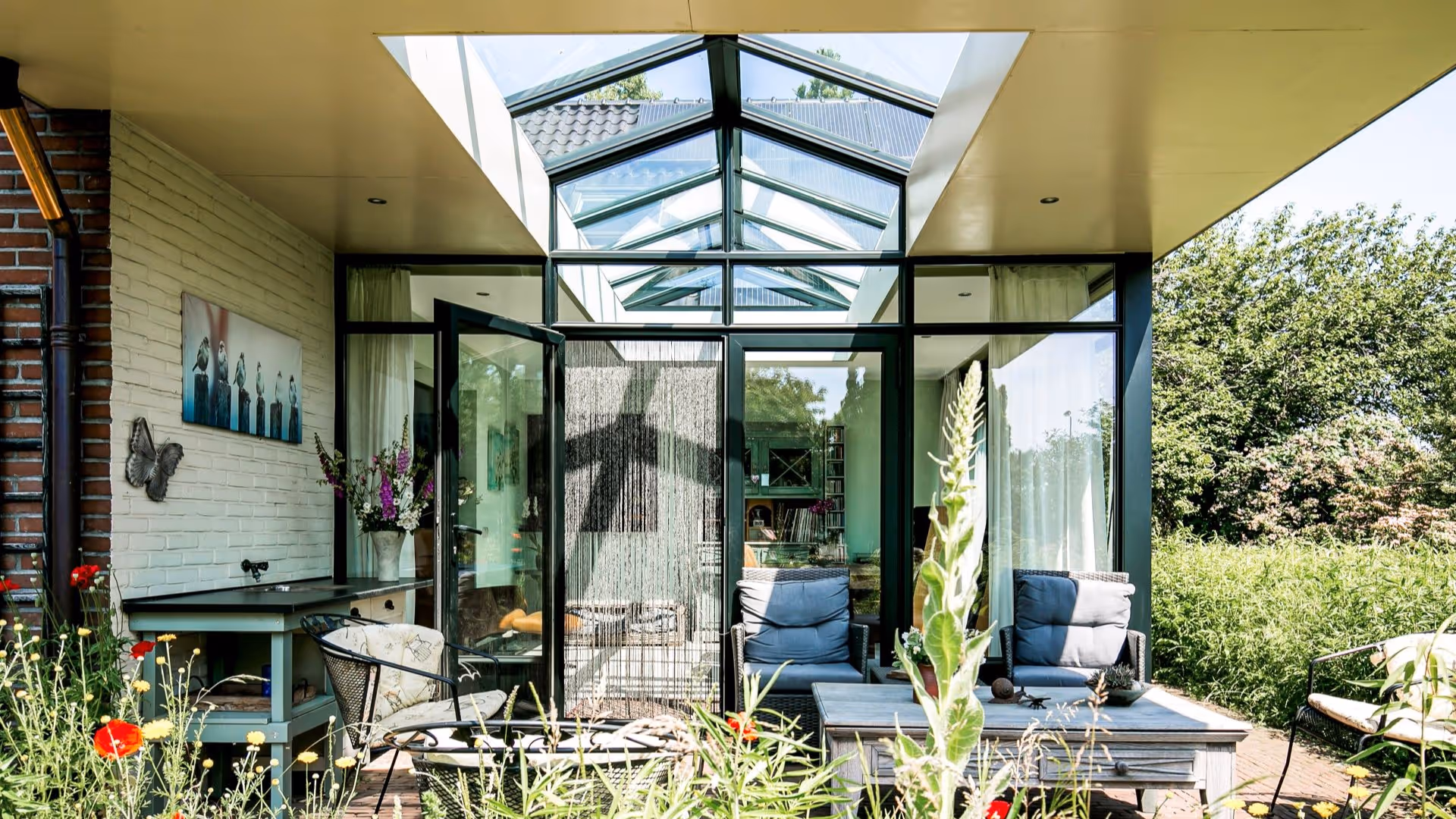 Glazen serre met moderne tuinmeubelen en ruime overkapping aan woning