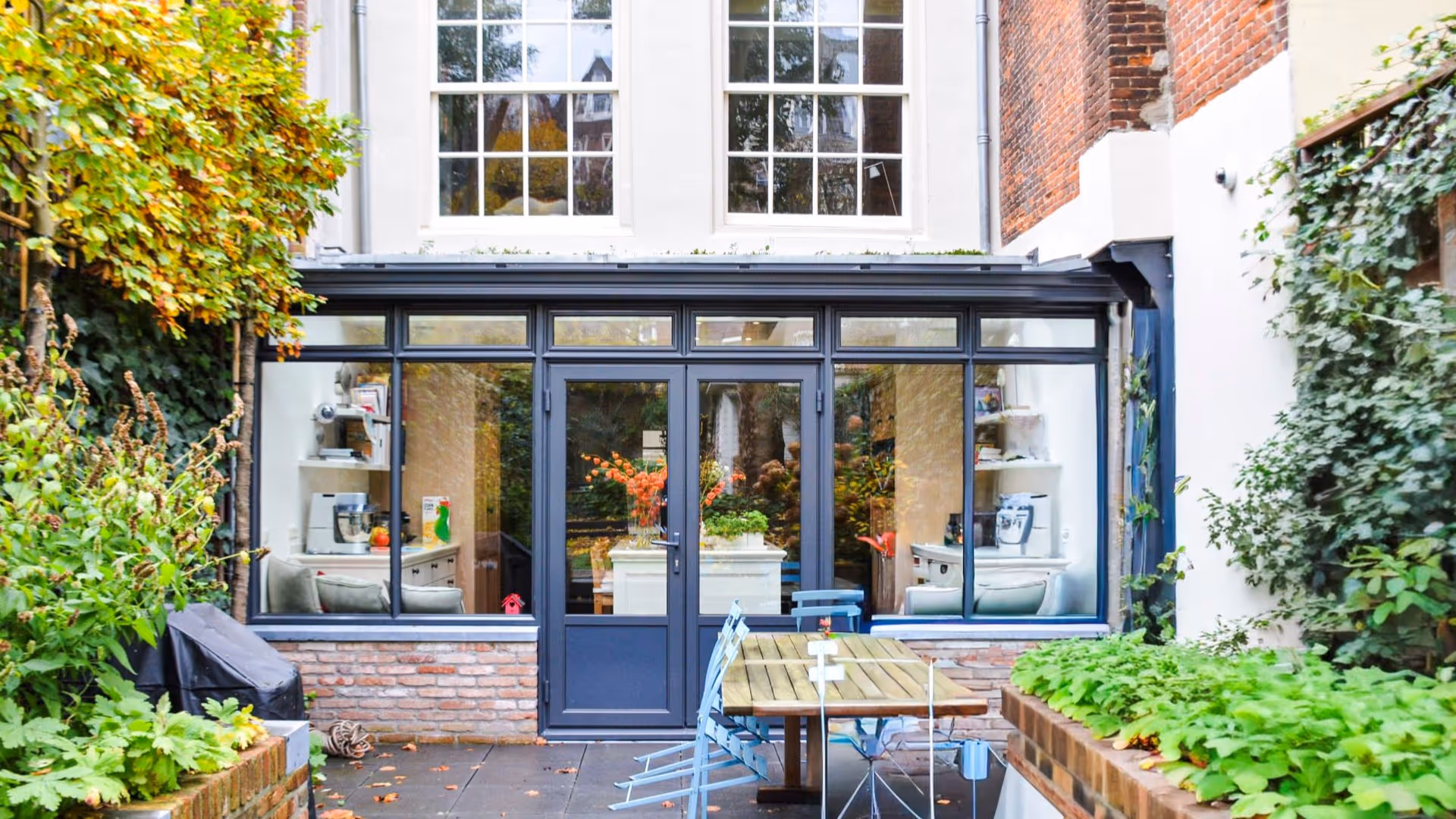 Moderne glazen serre aanbouw met ruim terras en groene binnentuin