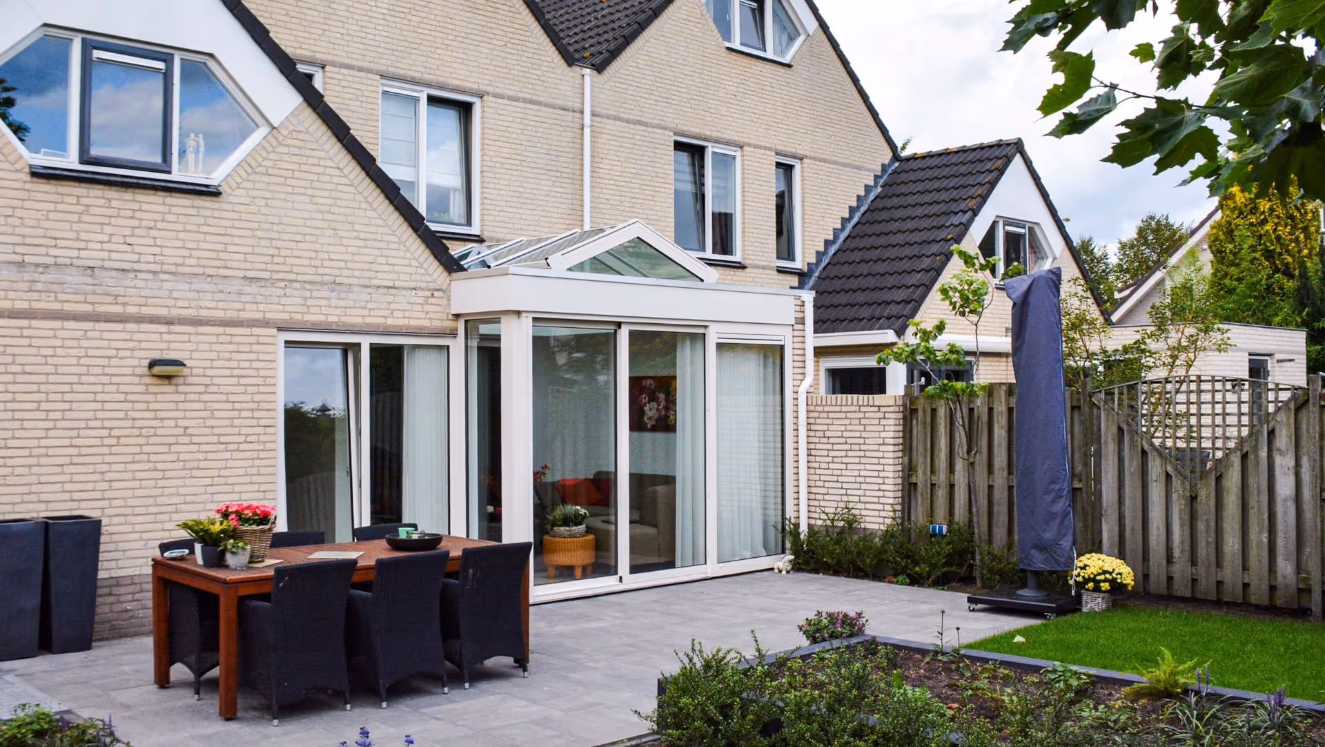 Moderne woning met witte serre aanbouw en ruim terras in verzorgde tuin