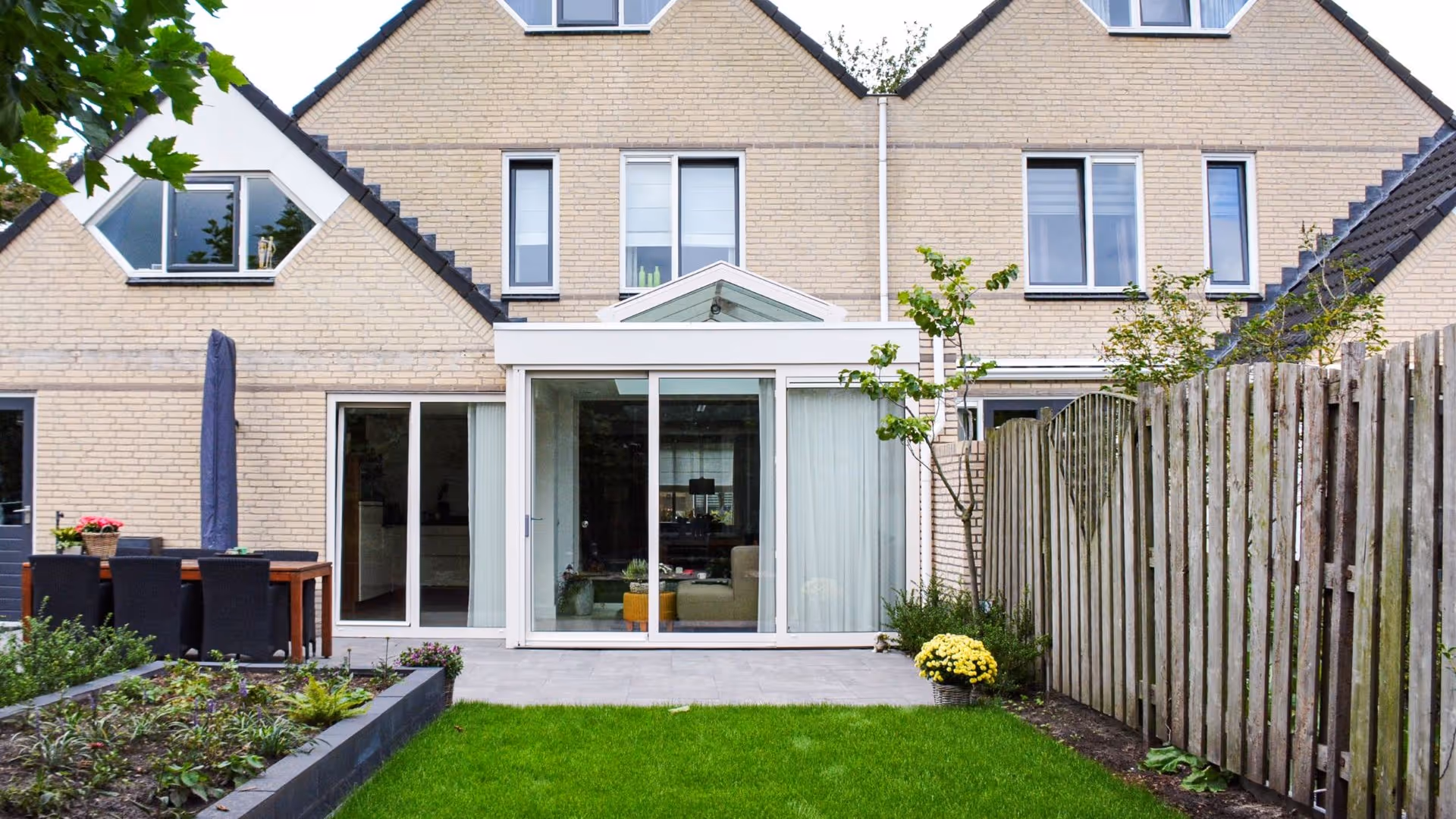 Strakke serre aan moderne woning met groene tuin en ruime glazen pui
