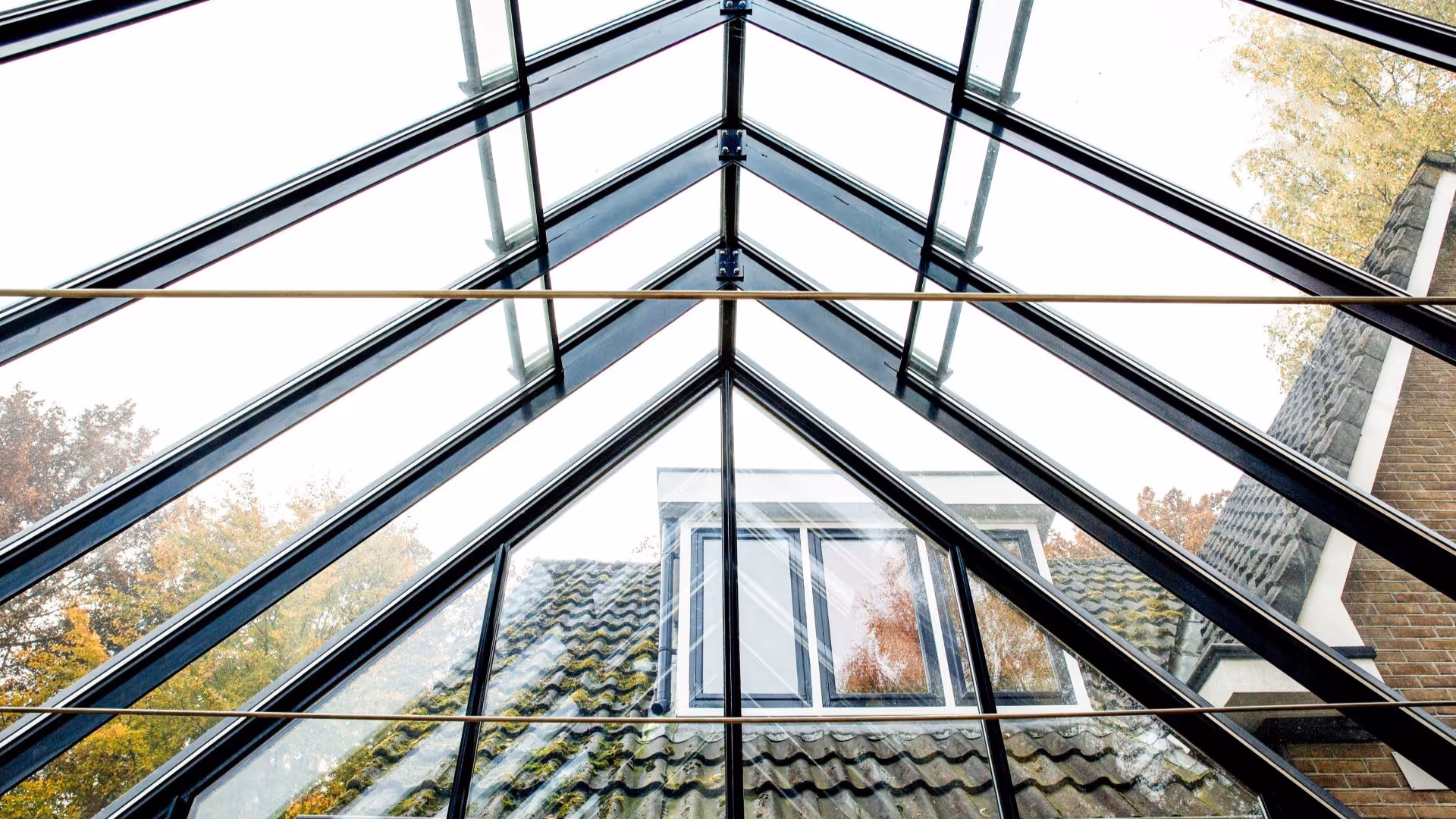 Binnenaanzicht van glazen uitbouw met zichtbaar zadeldak en uitzicht op woning