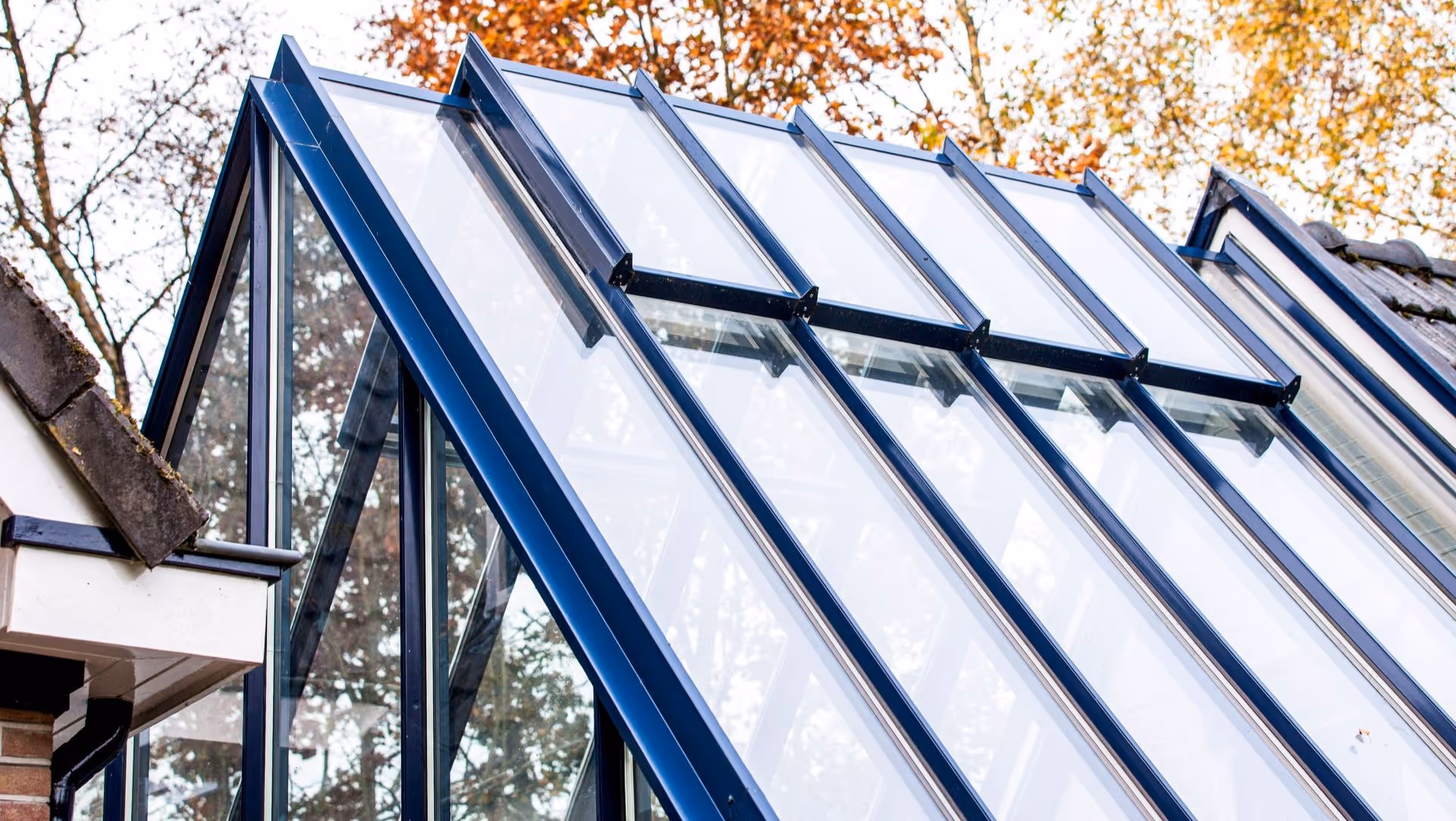 Moderne glazen aanbouw met zwart stalen frame en schuin dak aan landelijke woning