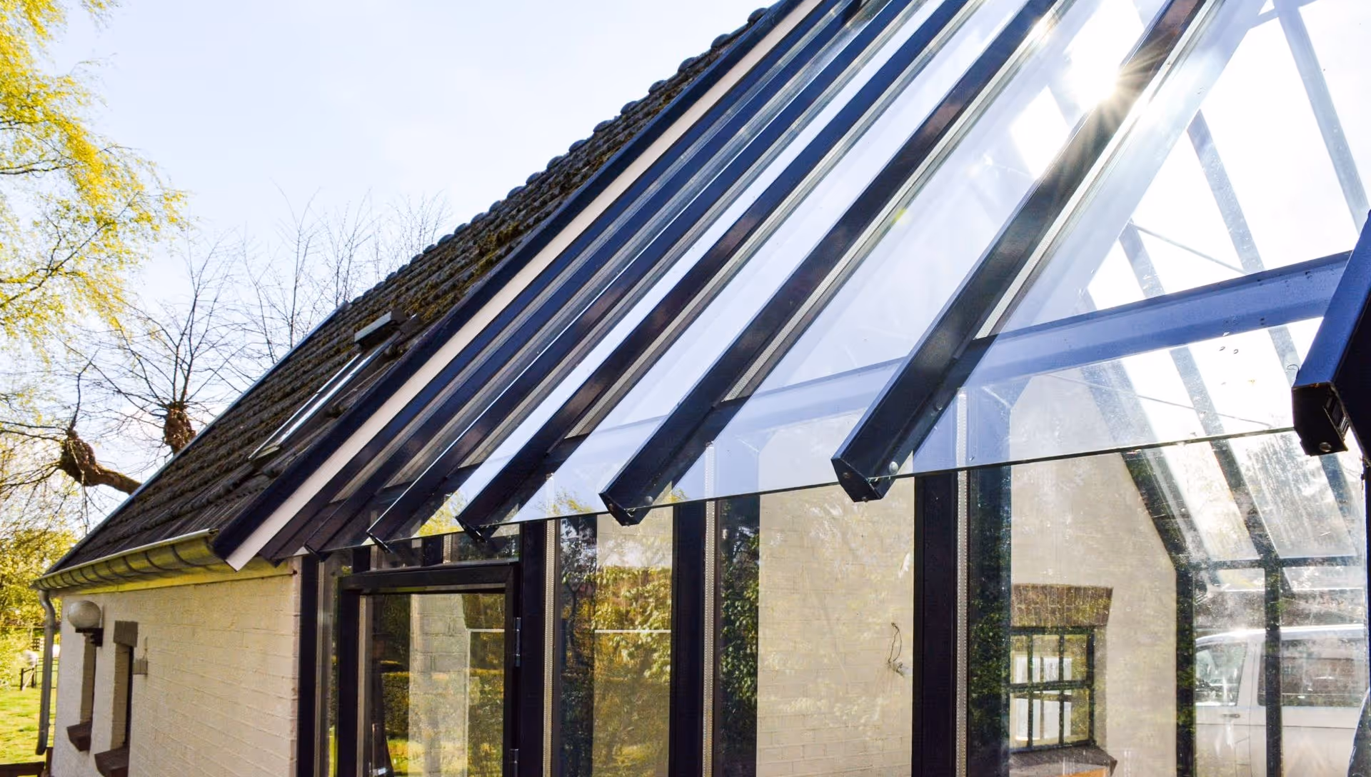 Zwarte aluminium uitbouw met glazen dak aan landelijke woning in groene omgeving