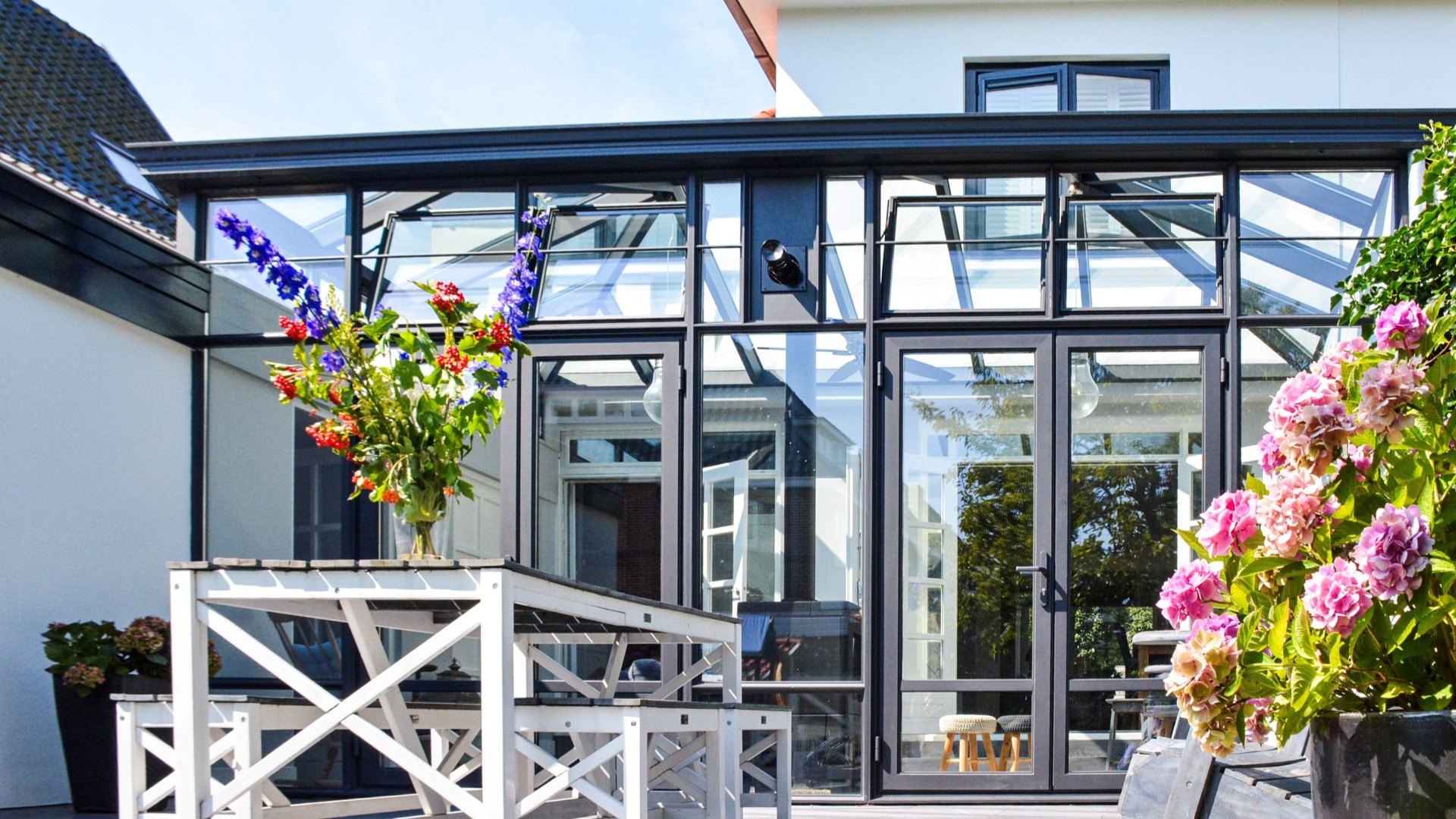 Stijlvolle steellook aanbouw met bloemen, glazen wanden en zwart aluminium frame.