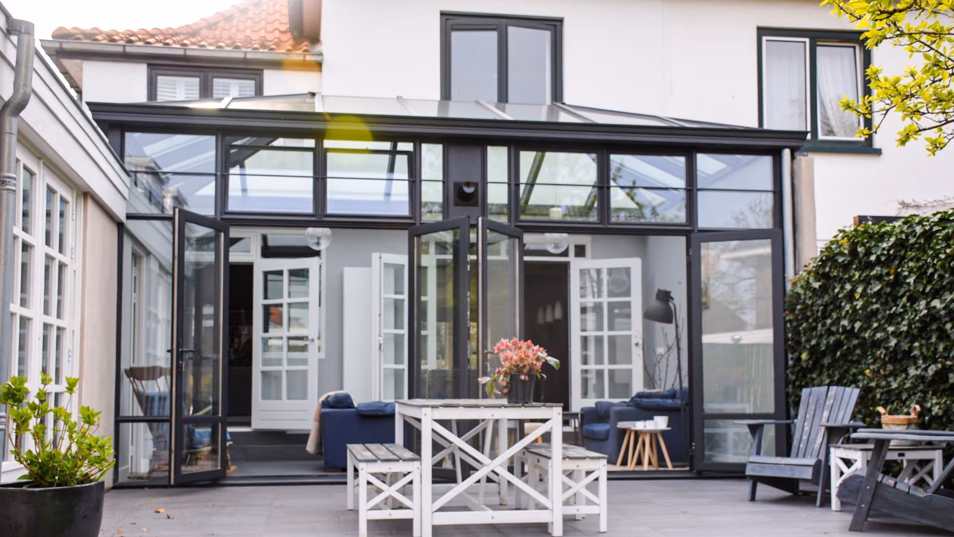 Moderne steellook woonuitbreiding met glazen dak en slanke zwarte aluminium profielen.