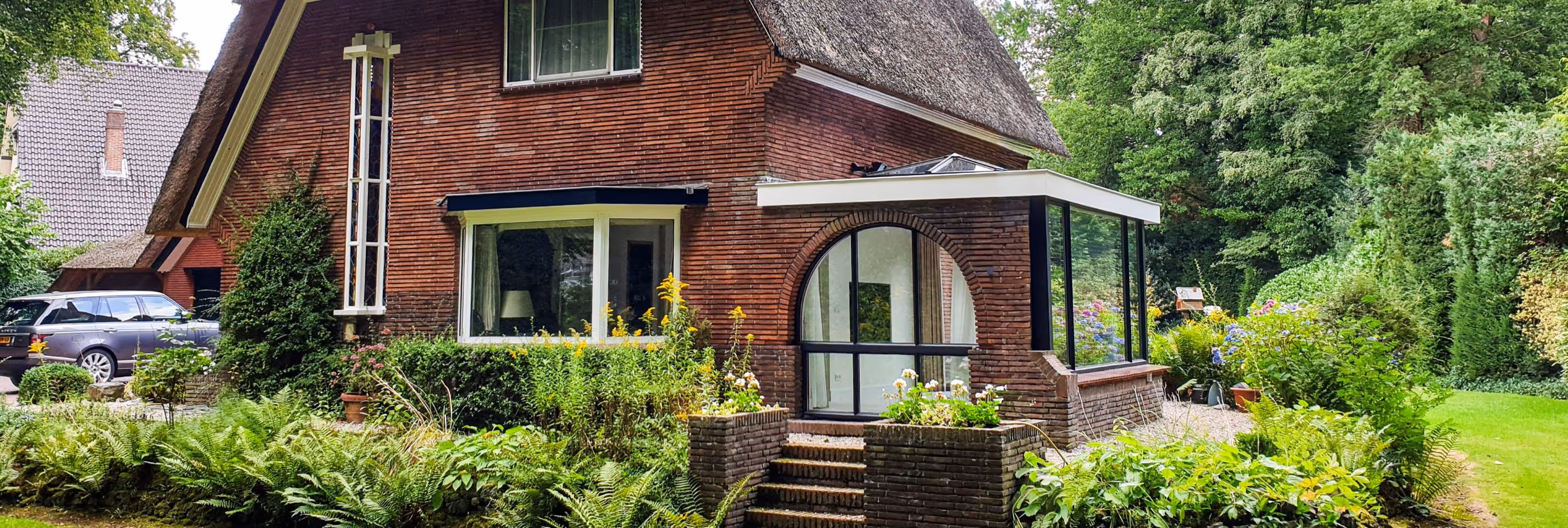 Serre steellook Doorwerth - Vrijstaande woning met moderne serre-aanbouw, grote glaspartijen en groene tuin rondom.