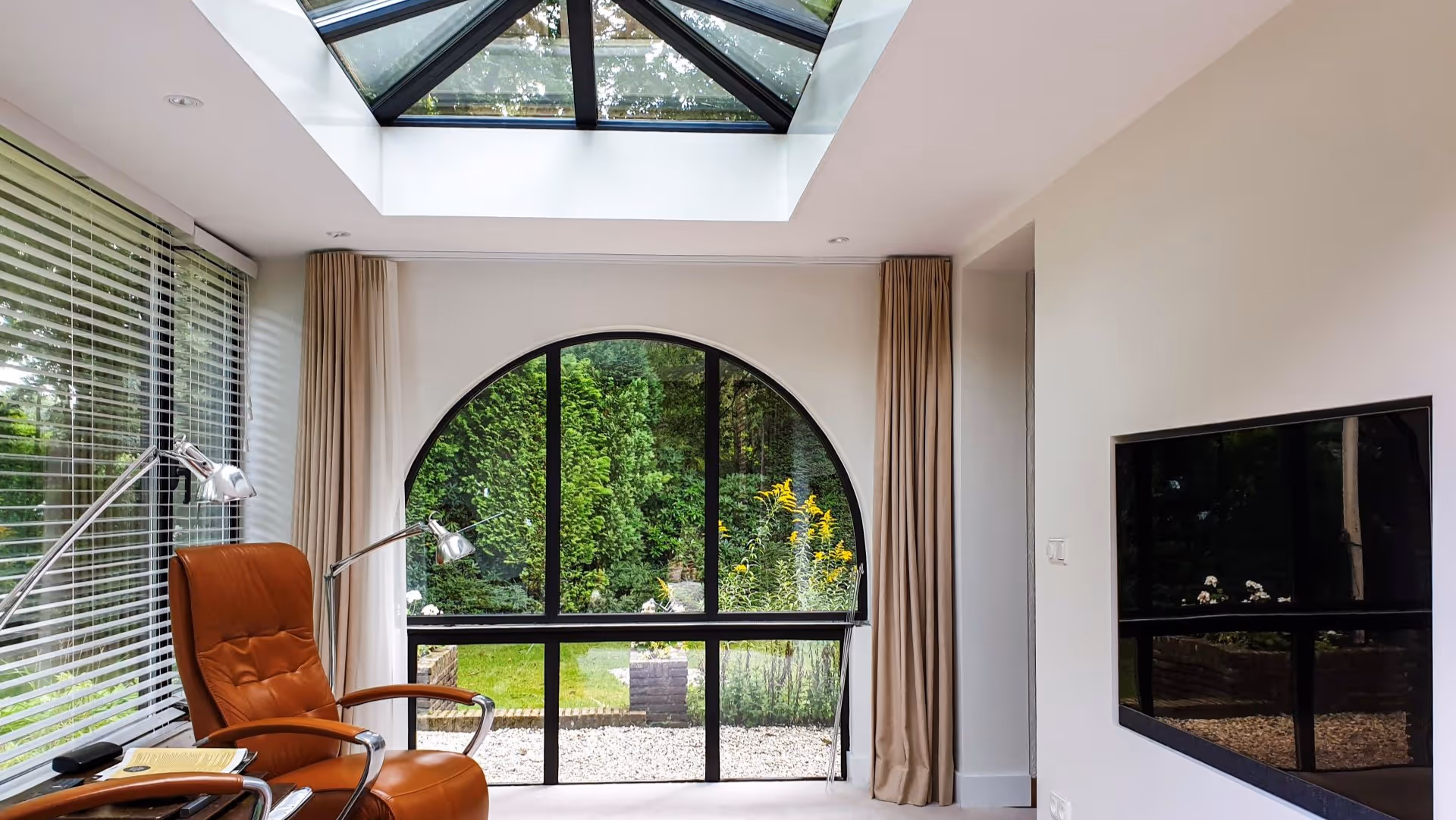 Interieur van moderne serre met veel daglicht, zwart aluminium frame en uitzicht op groen.
