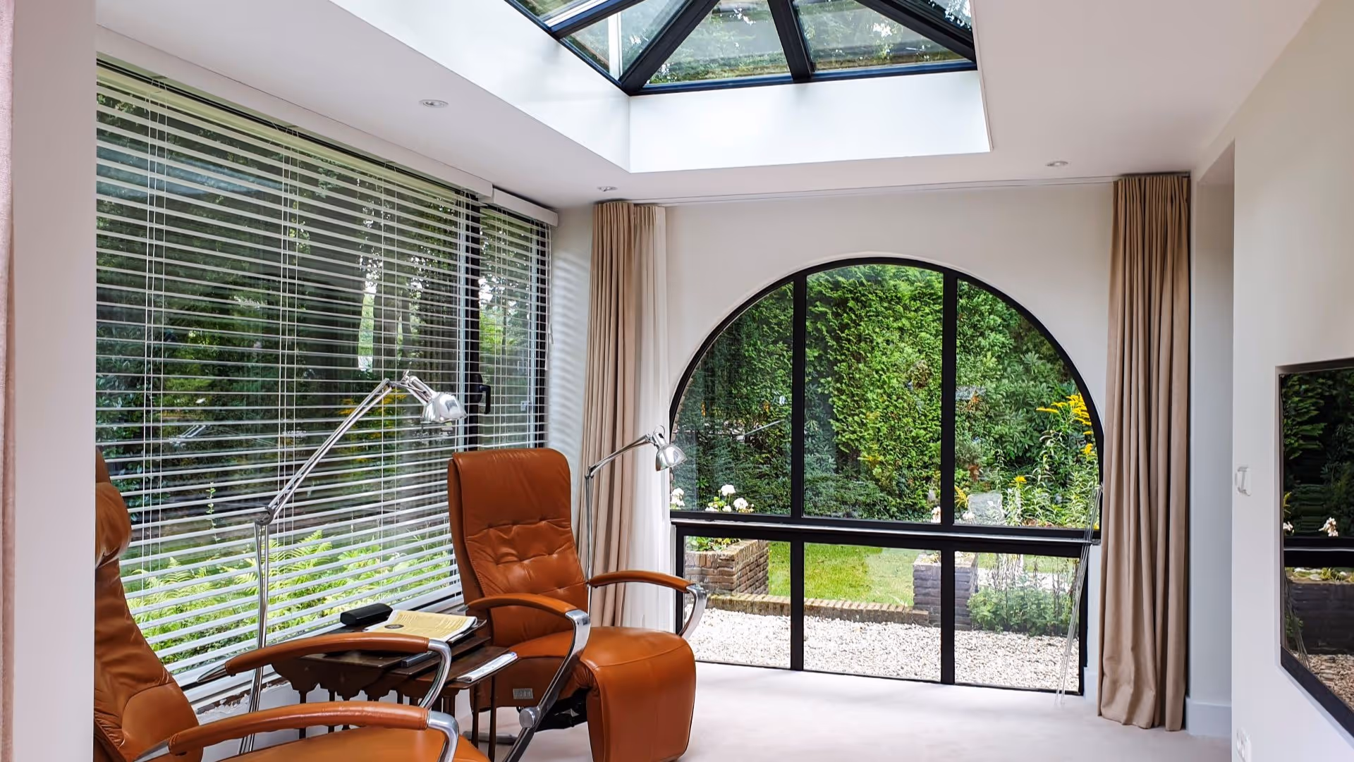 Moderne tuinkamer met glazen lichtstraat, comfortabele zitruimte en halfrond raam.