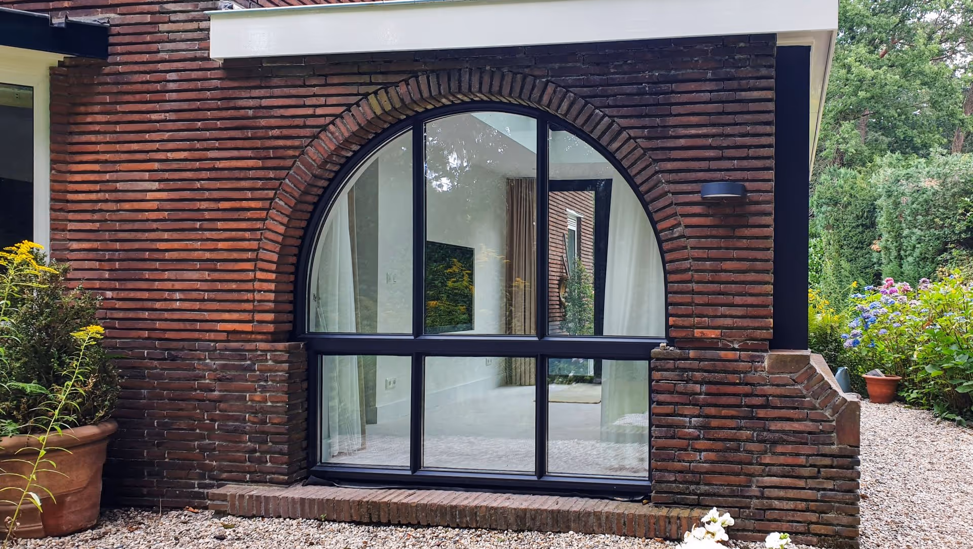 Karakteristieke aanbouw met halfrond raam, donkere kozijnen en gemetselde boogconstructie.