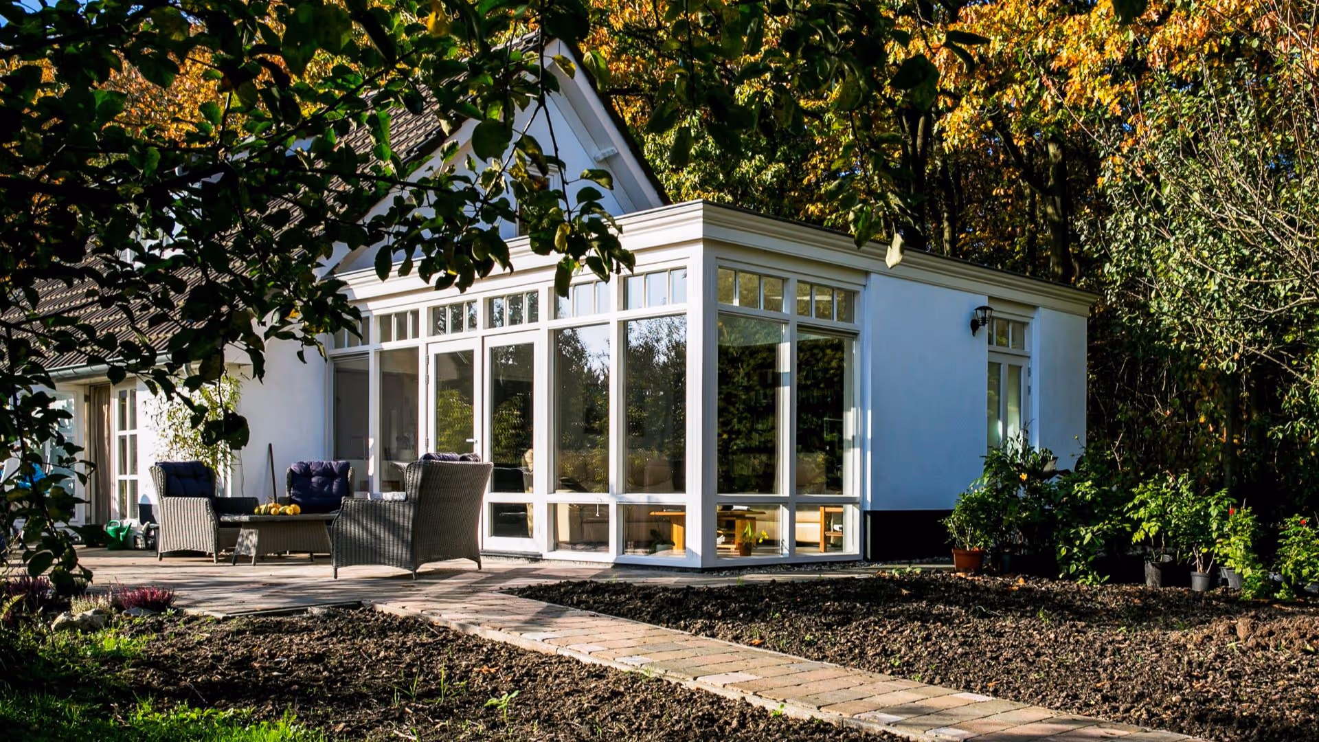 Klassieke aanbouw met witte kozijnen, royale ramen en zonnig terras in groene tuin.