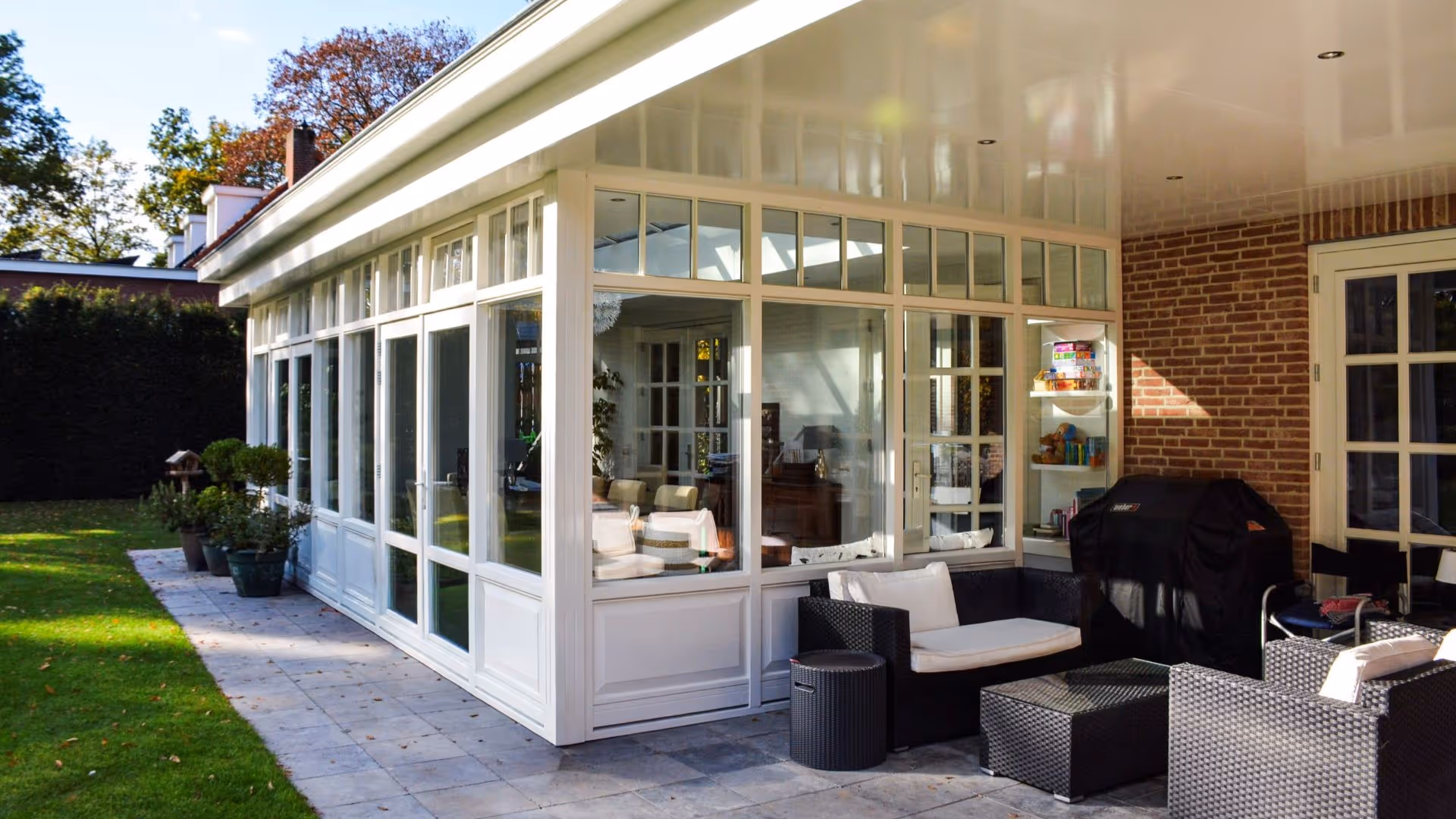 Witte aluminium serre met overdekt terras en grote glaspartijen aan luxe woning.
