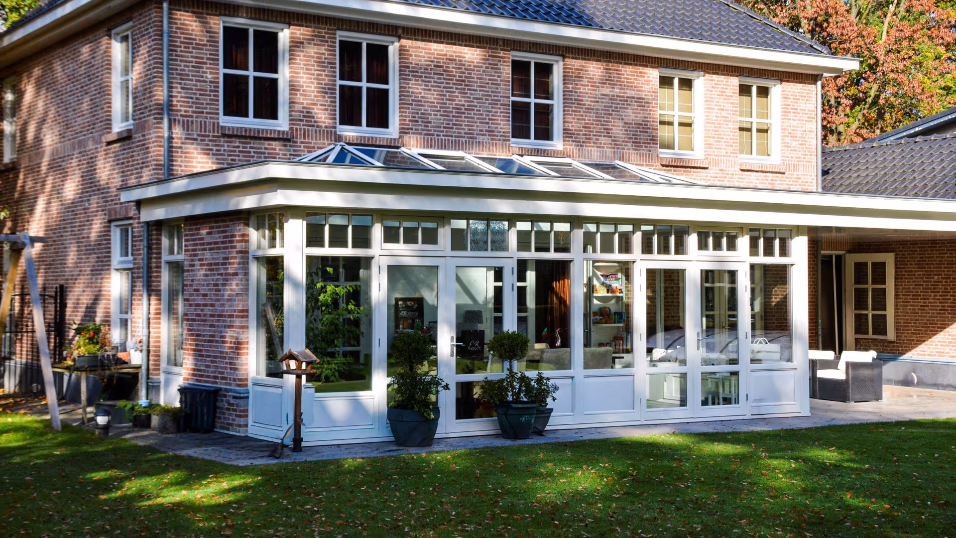 Ruime landelijke serre met witte kozijnen, glazen lichtstraat en uitzicht op de tuin