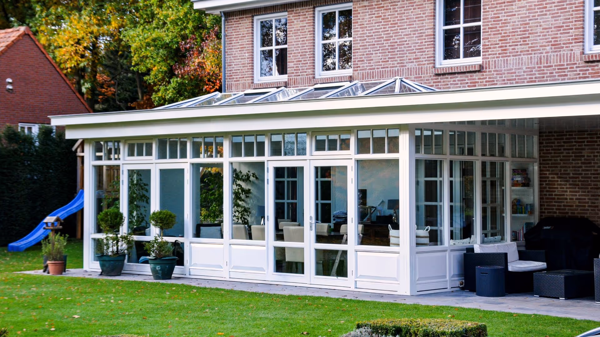 Overdekte terrasserre met witte kozijnen, glazen lichtstraat en uitzicht op de achtertuin.