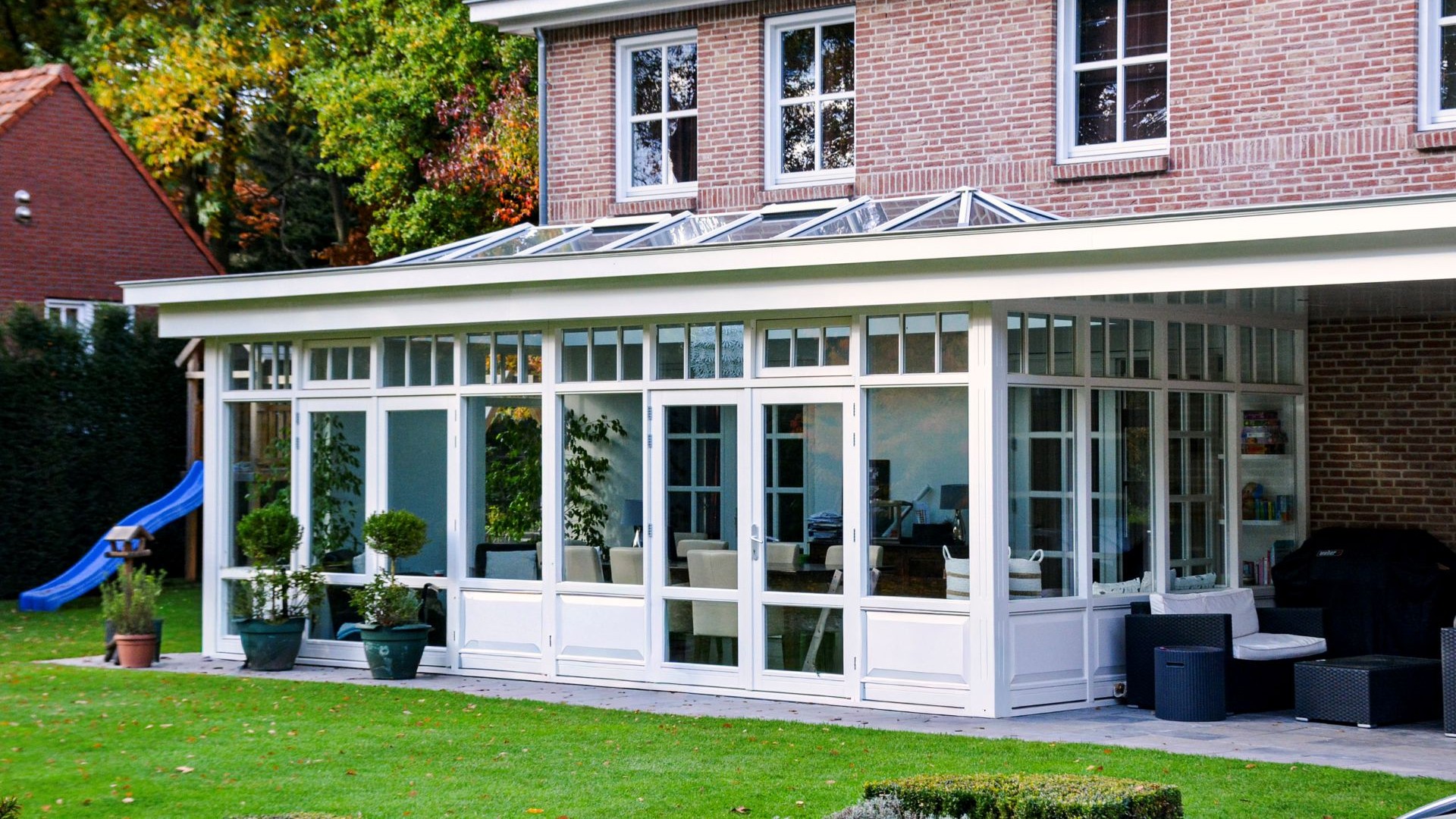 Overdekte terrasserre met witte kozijnen, glazen lichtstraat en uitzicht op de achtertuin.