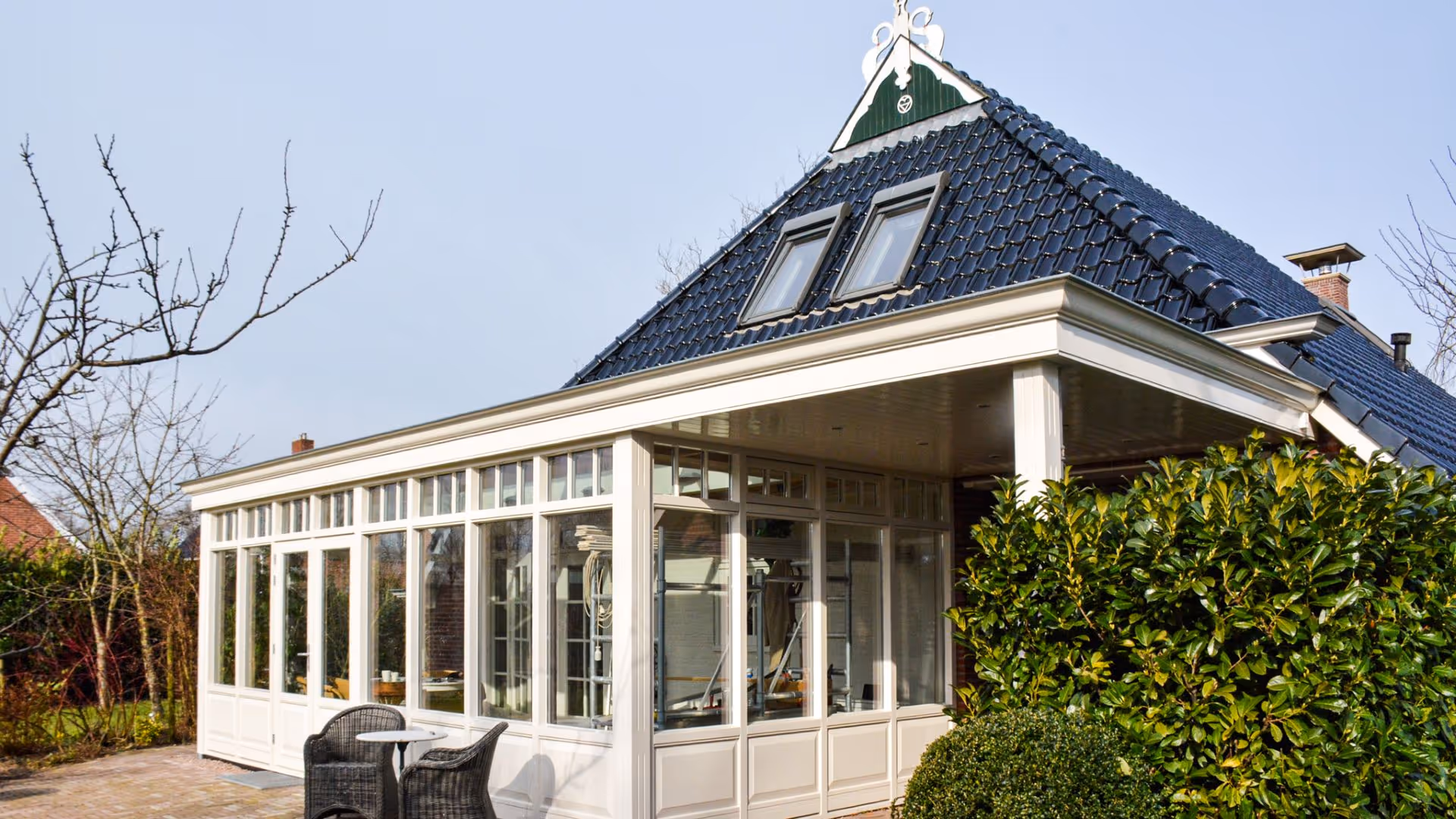 Klassieke witte serre met overkapping en grote glaspartijen als verlengstuk van de woning.