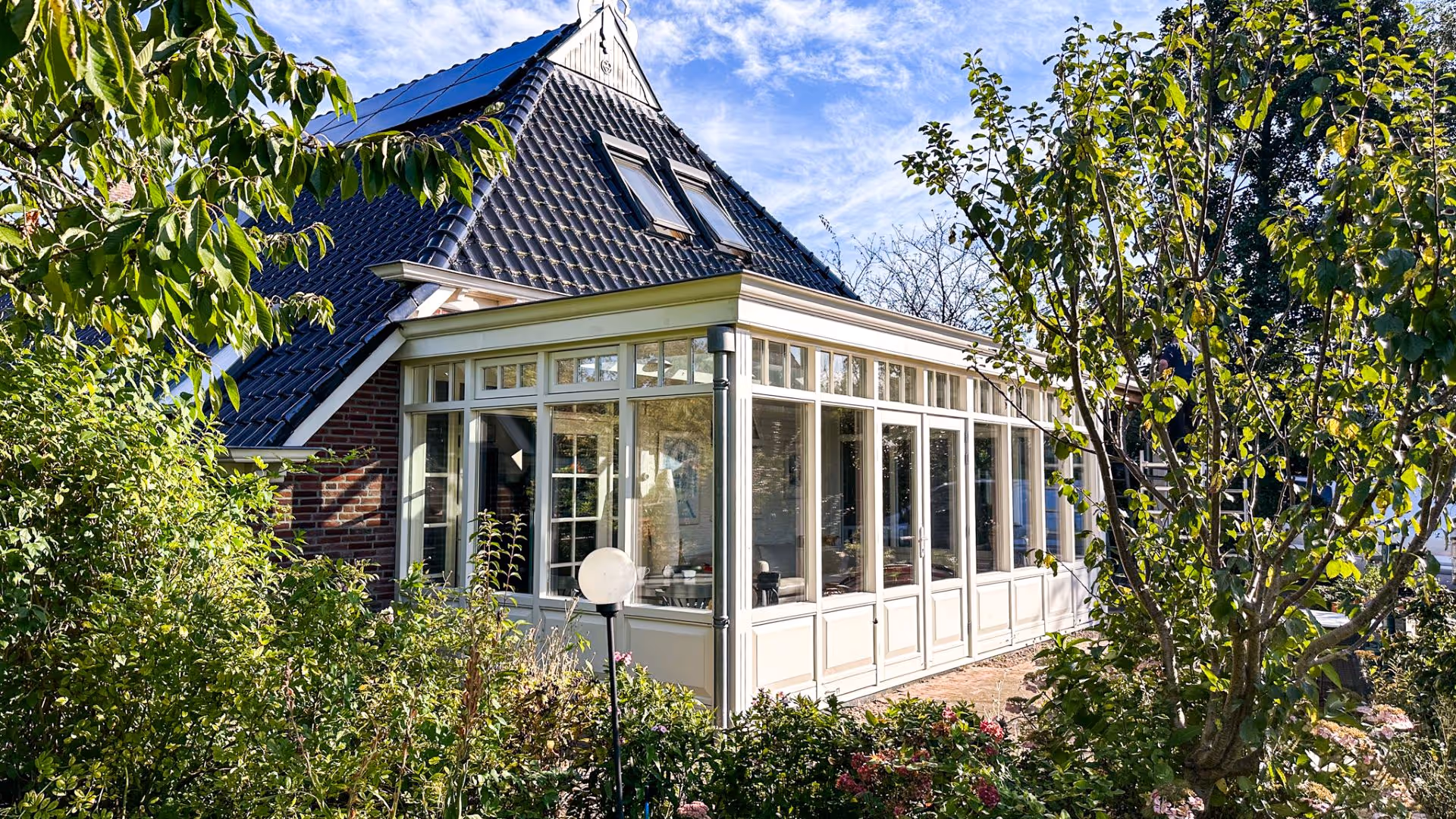 Buitenzijde van klassieke witte serre met hoge glaspartijen en openslaande deuren.