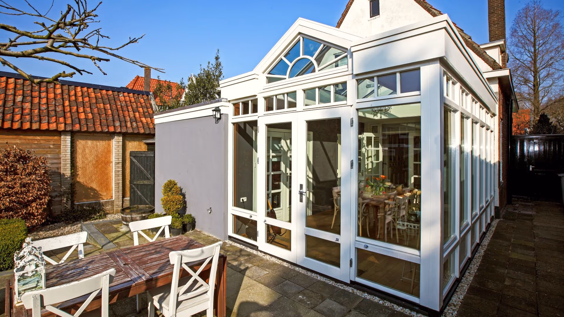 Witte serre met karakteristieke glasgevel en hoge ramen, geplaatst aan de achterzijde van de woning.