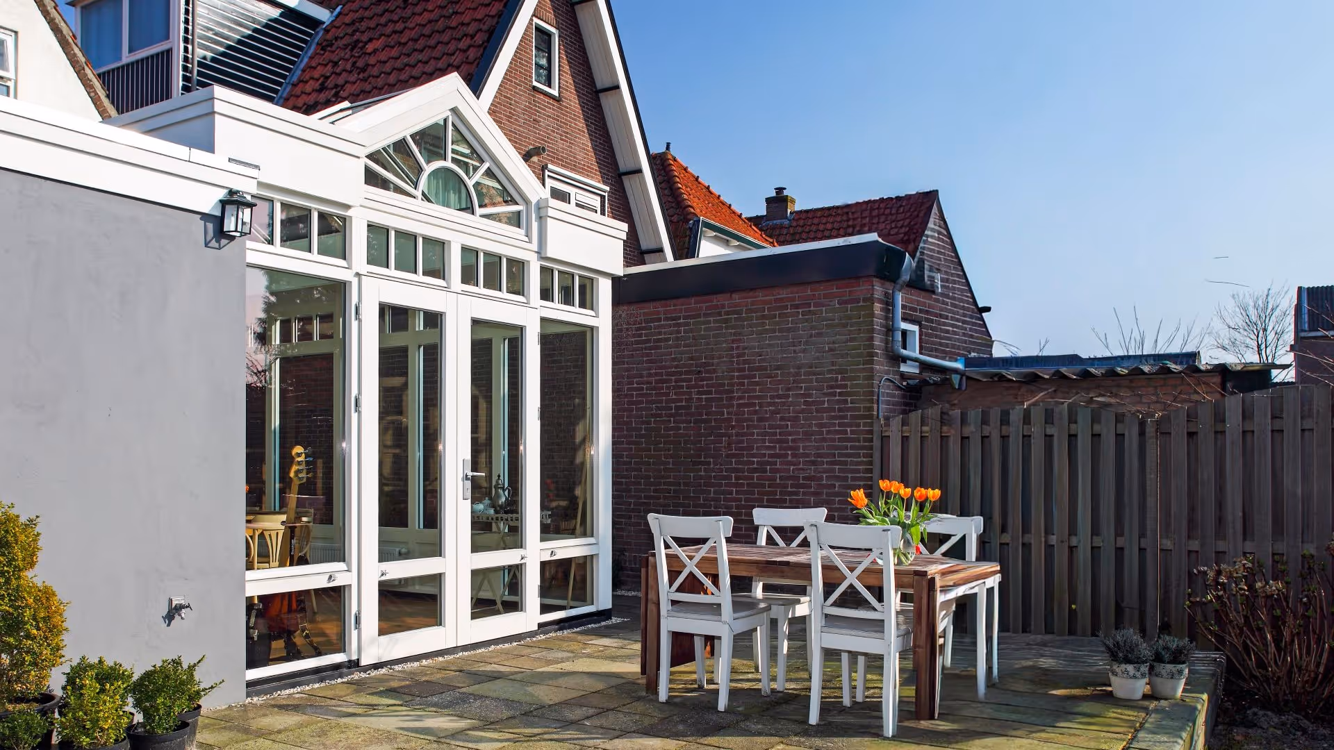 Ruime glazen aanbouw met klassieke detaillering, openslaande deuren en terras aan de tuin.