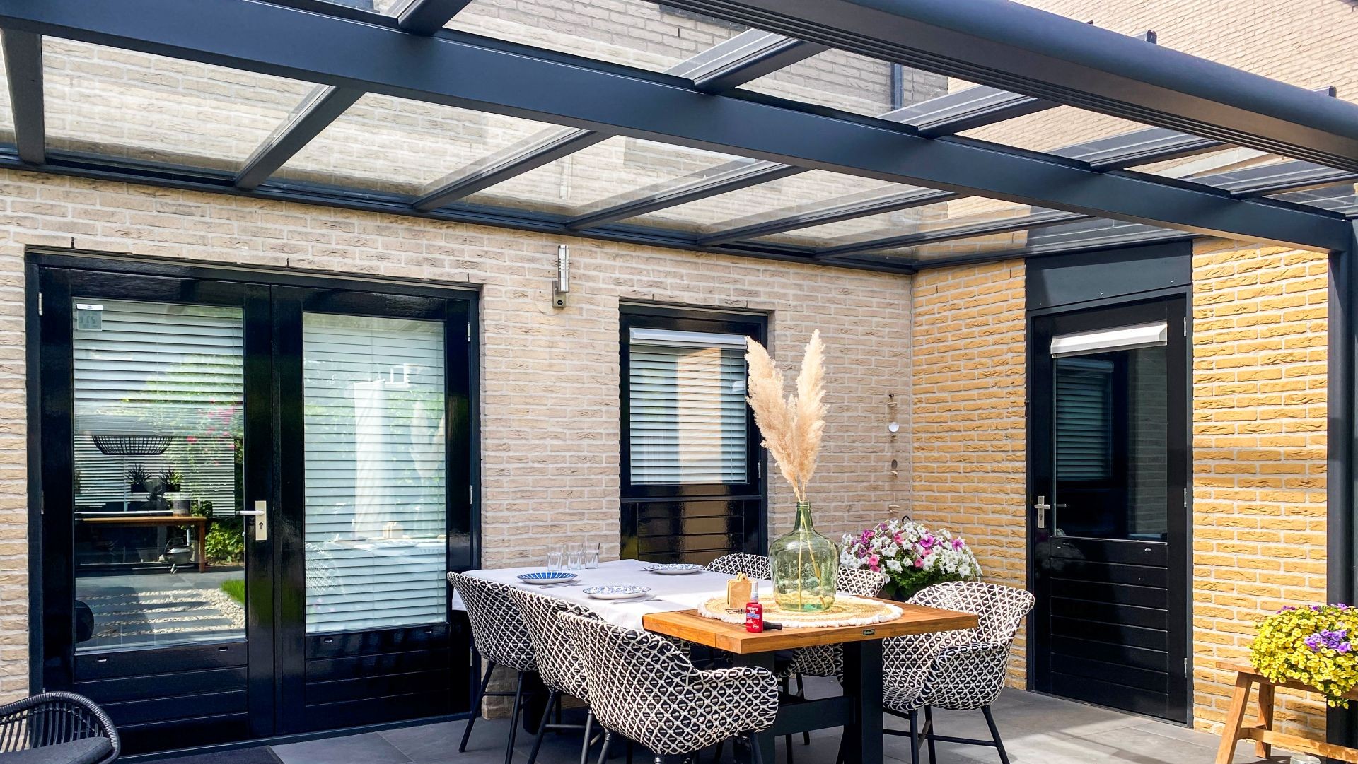 Ruime terrasoverkapping met glazen schuifwanden, eettafel en bloeiende planten in tuin