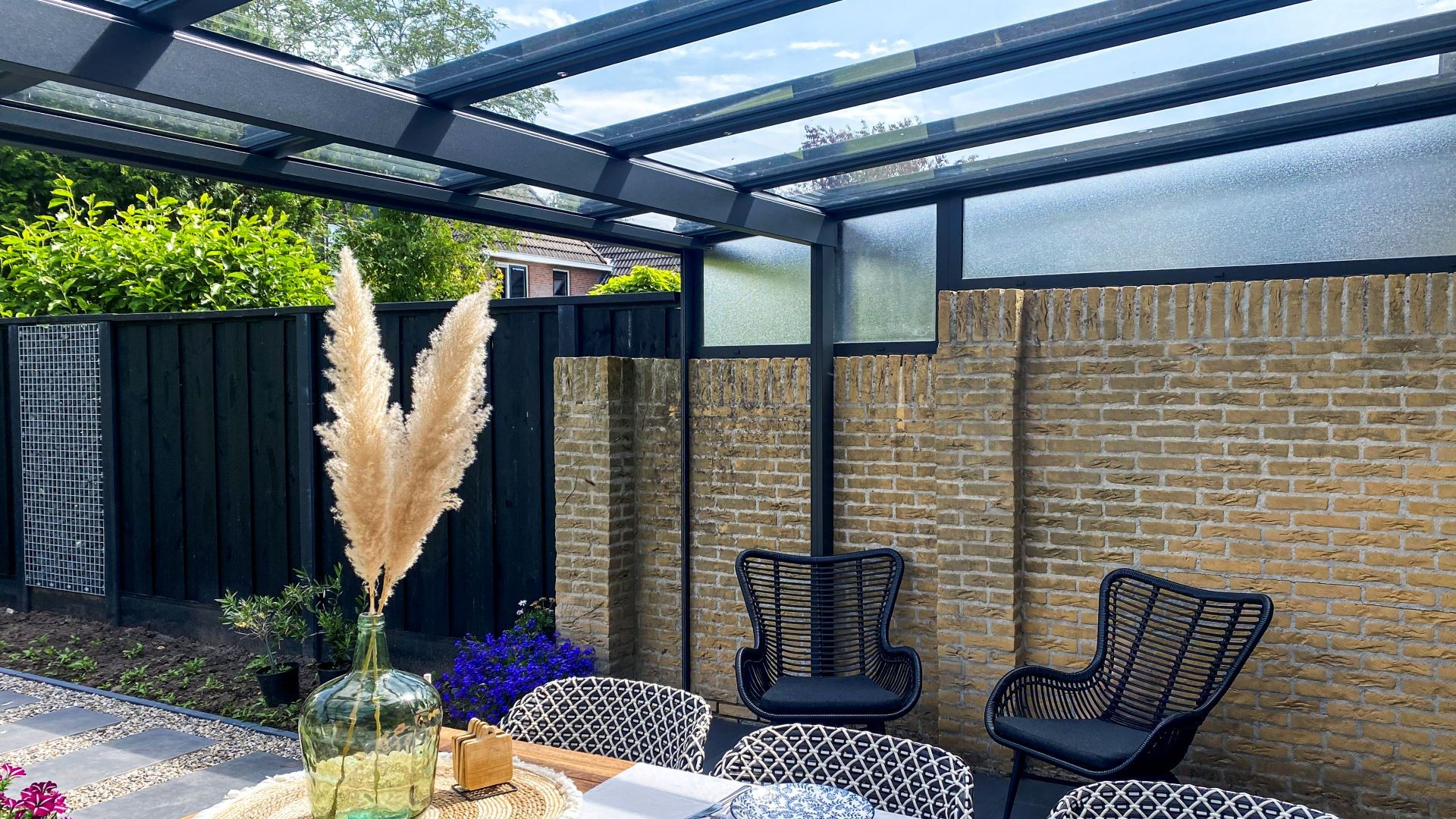 Uitzicht vanuit terrasoverkapping met volledig geopende glazen schuifwanden naar groene tuin