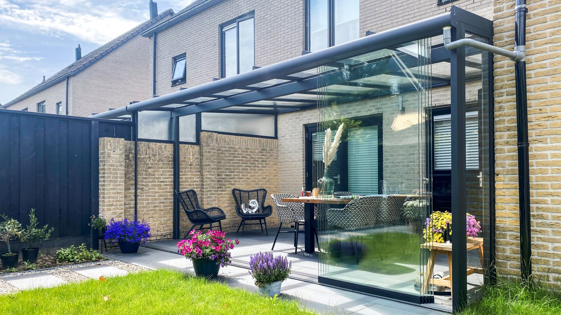 Overdekt terras met glazen zijwanden, moderne stoelen en onderhoudsvriendelijke bestrating