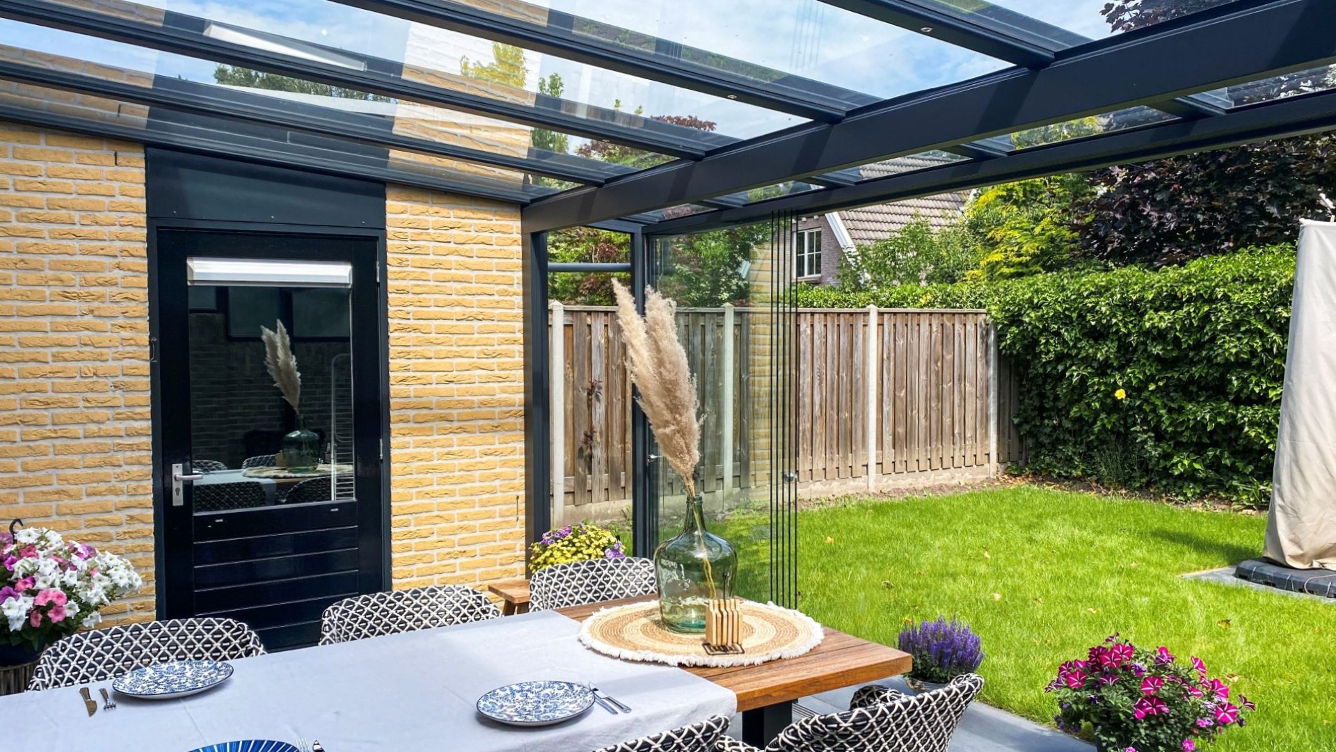 Detail van luxe terrasoverkapping met glazen dakconstructie en comfortabele tuinset